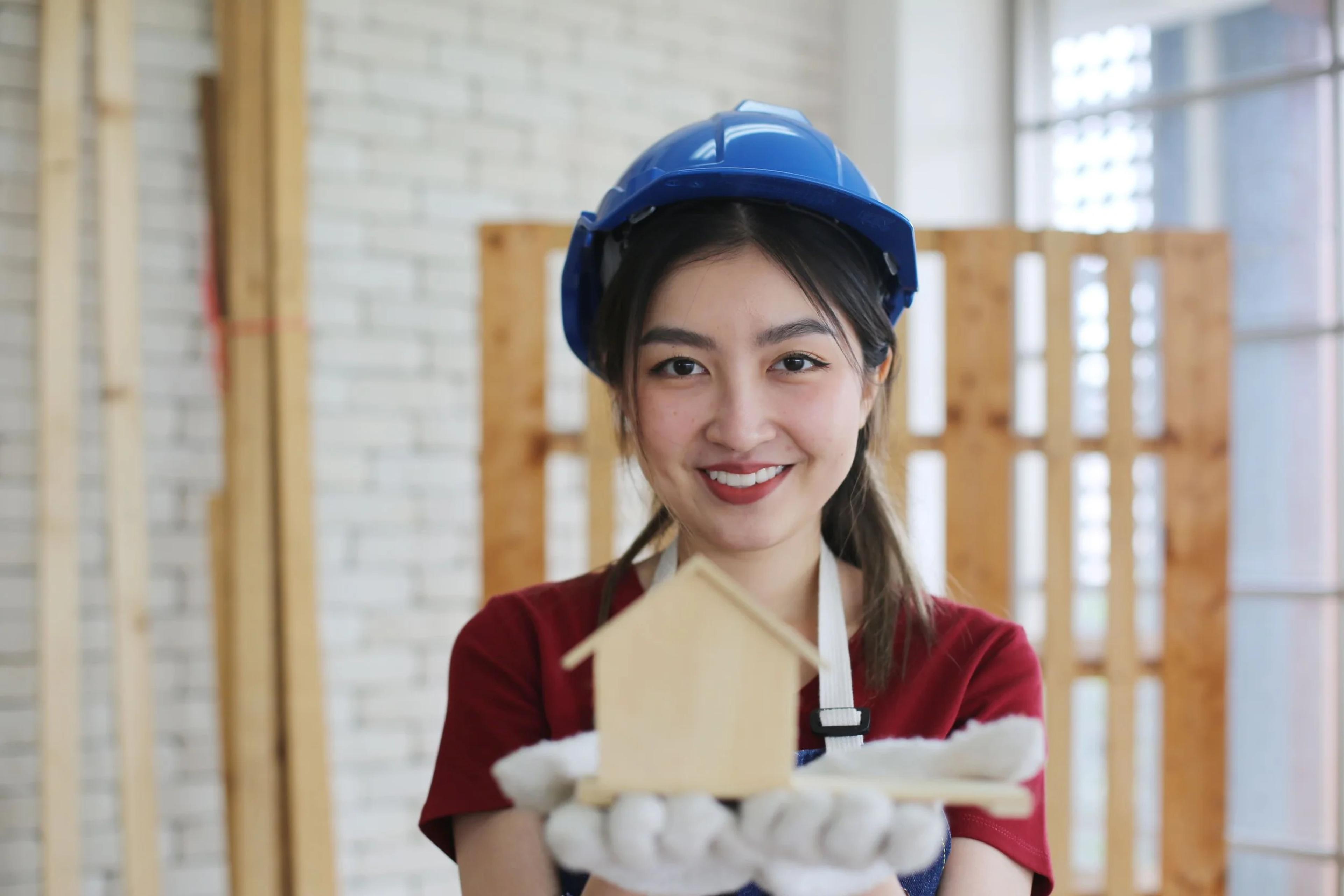 Smiling woman in a hard hat holding a small wooden house model