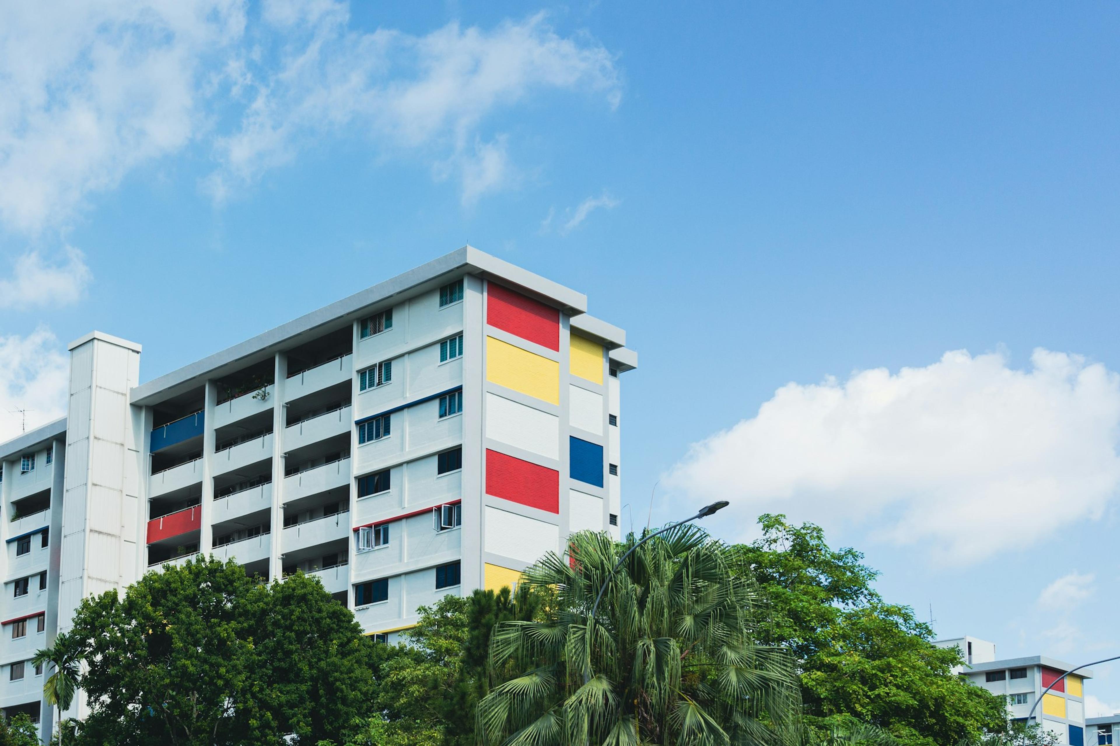 Colourful HDB block with palm trees in front, under a blue sky
