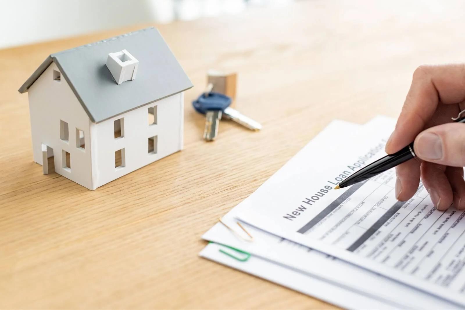 Filling in a new house loan application beside a model house and keys