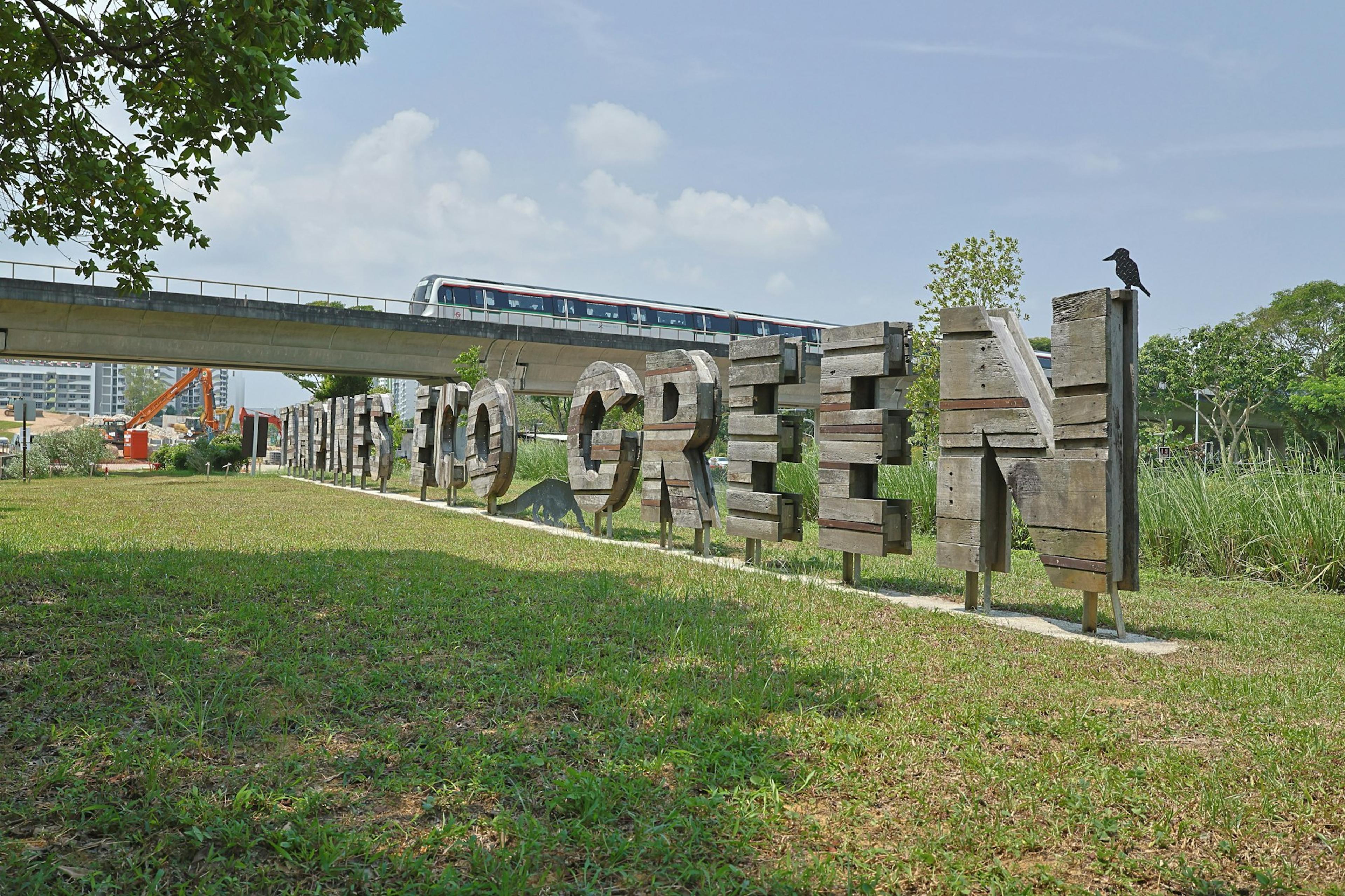 An MRT train passing the Tampines Eco Green sign beside a grassy field