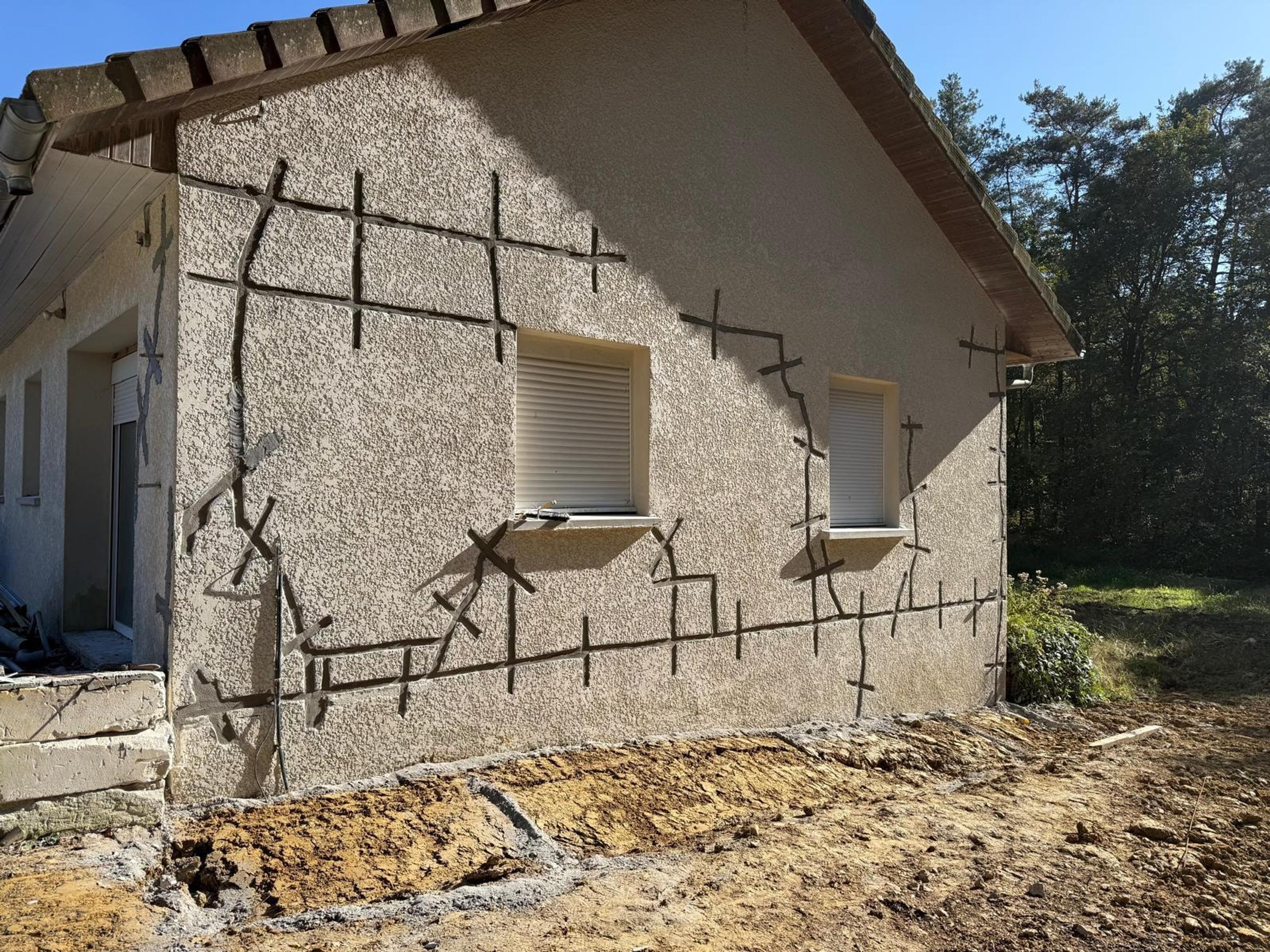 Pignon d’une maison crépie, fissures agrafées sur toute la façade