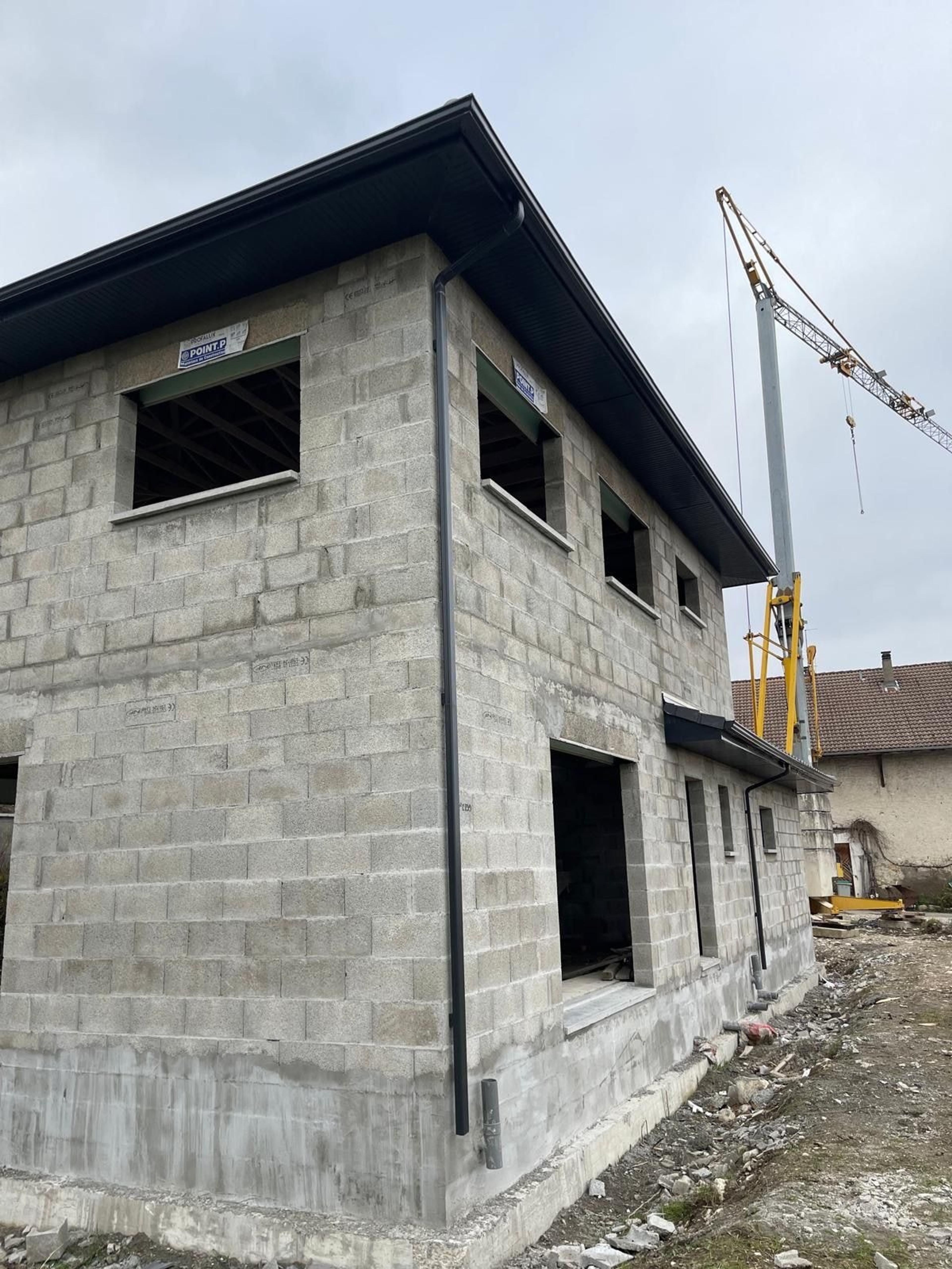 Maison à étage en blocs de béton, toiture posée, grue de chantier en arrière-plan