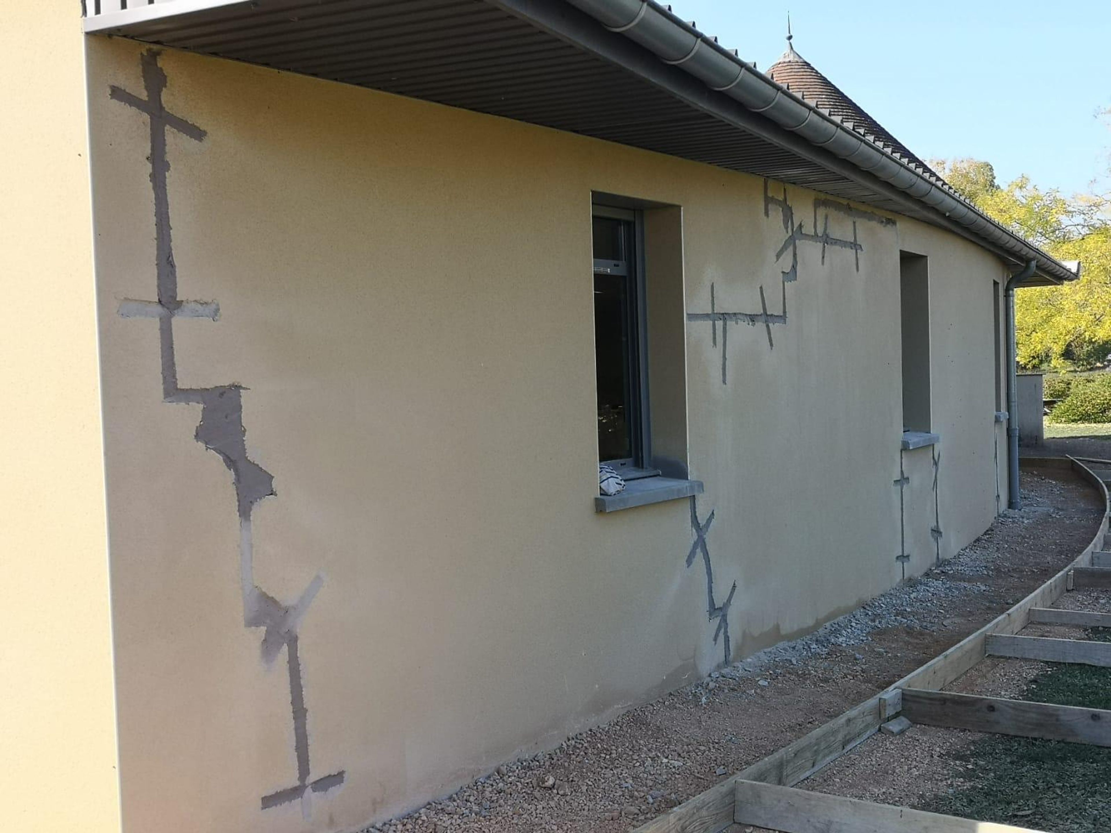 Façade aux fissures agrafées en cours de reprise, coffrage du trottoir au pied du mur
