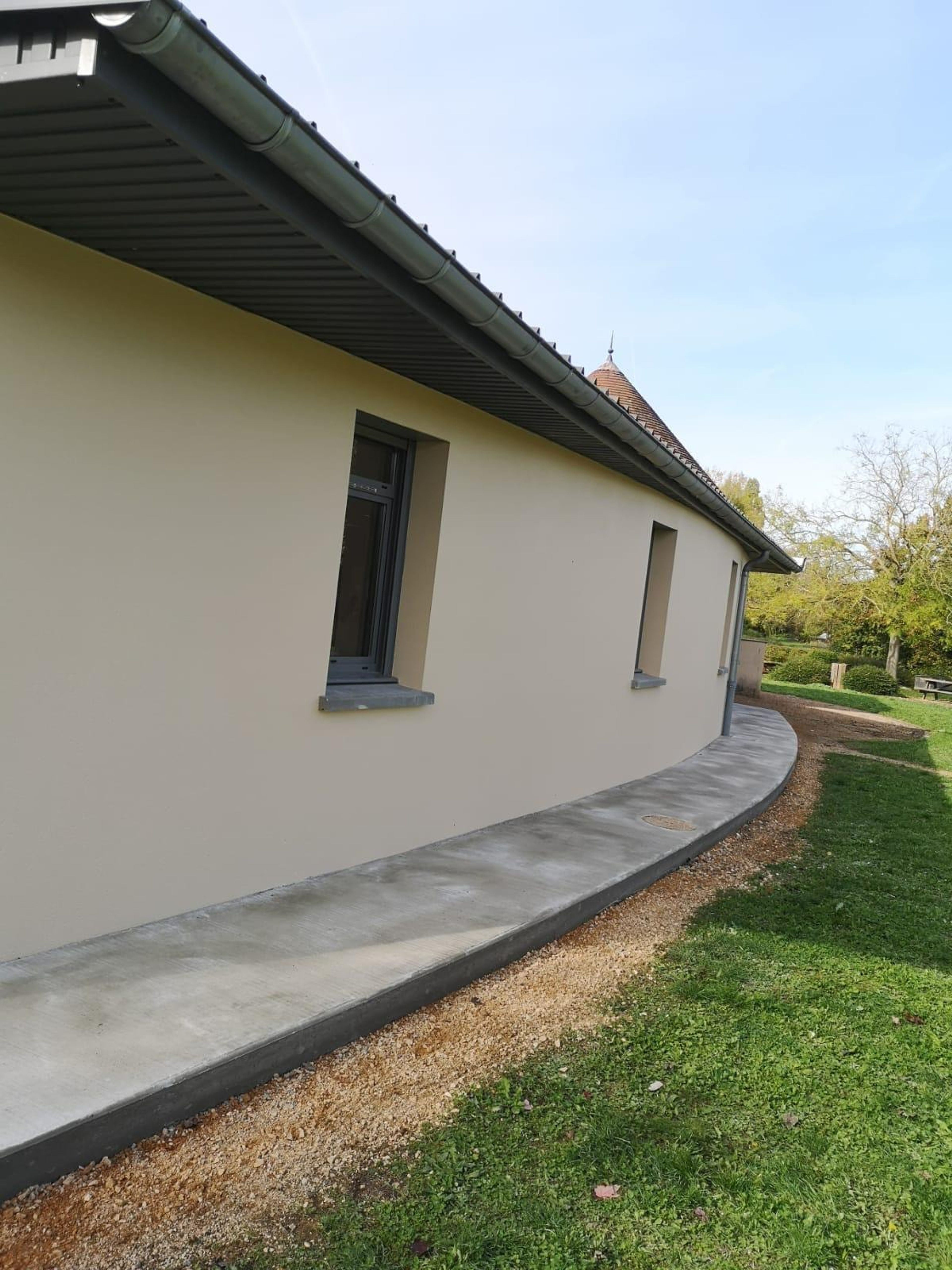 La même façade après les travaux : façade reprise et trottoir en béton le long du mur