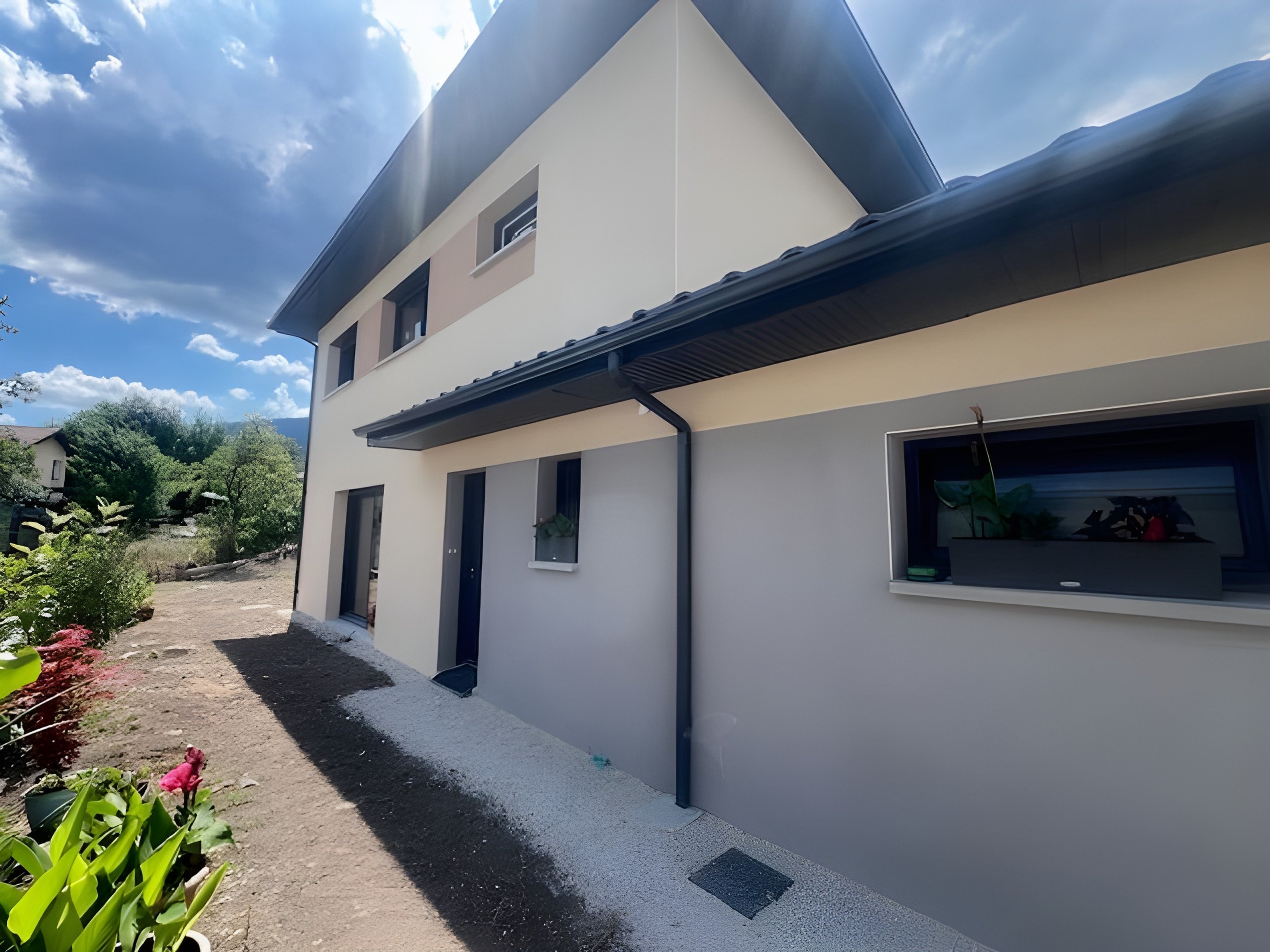 Maison contemporaine à étage à Péron : rez-de-chaussée gris sous l’auvent, garage et sa fenêtre en bandeau