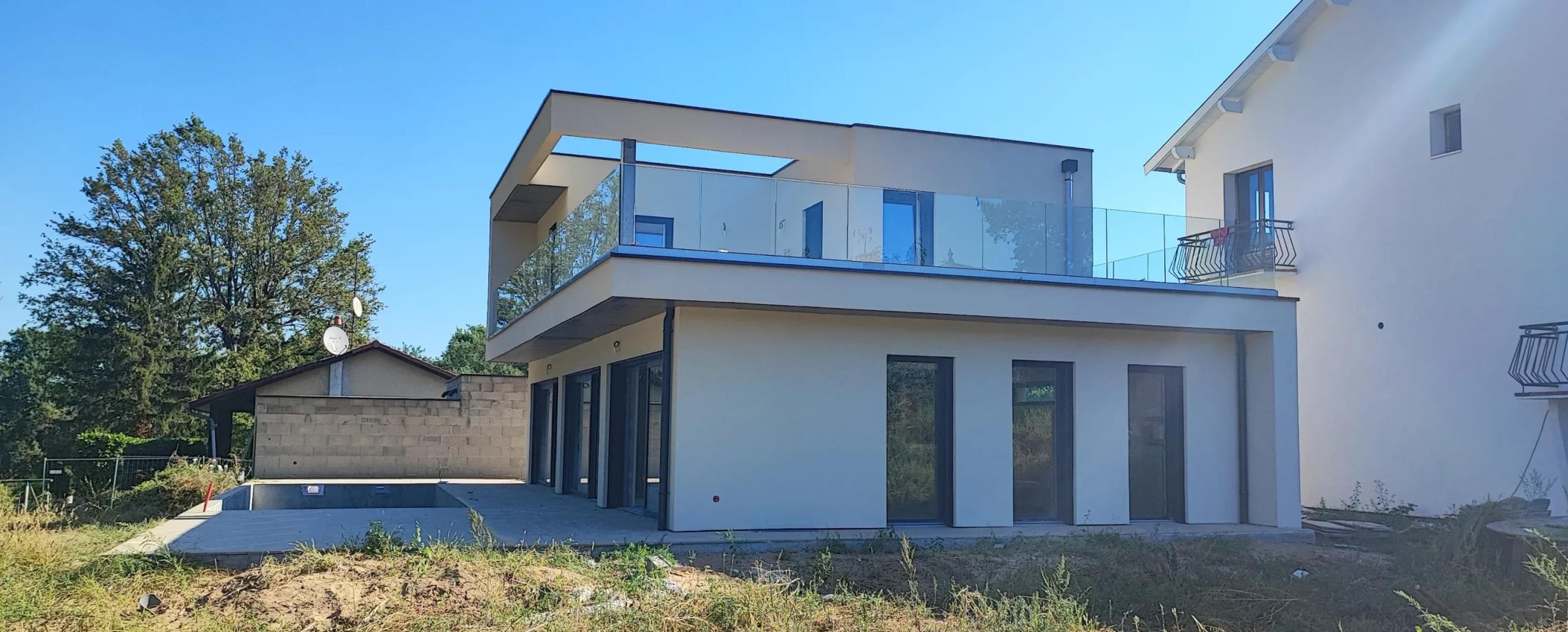 La maison en fin de chantier : toit plat, terrasse à garde-corps vitrés, baies vitrées et piscine