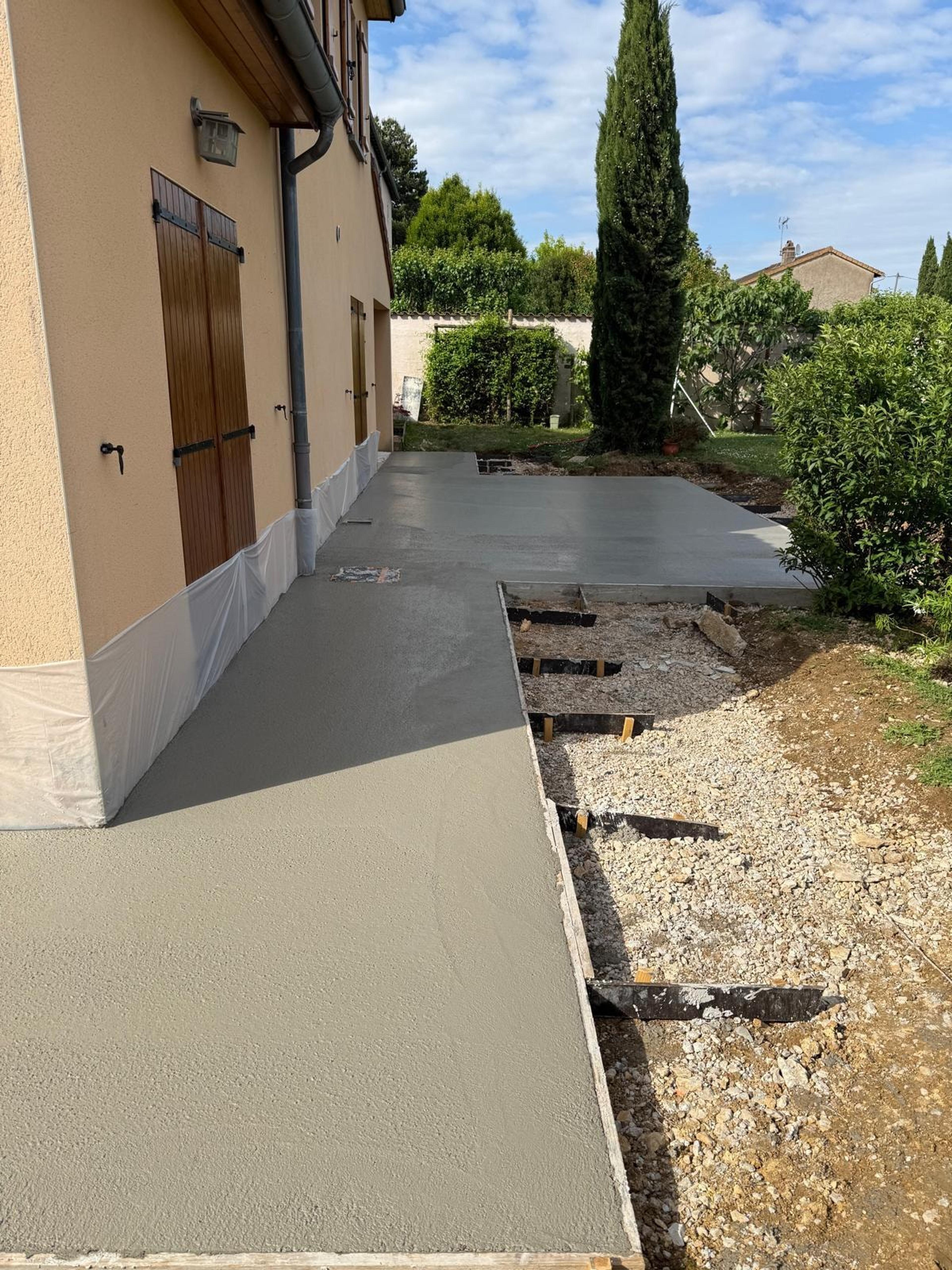 Trottoir en béton fraîchement coulé au pied d’une maison, coffrages en place