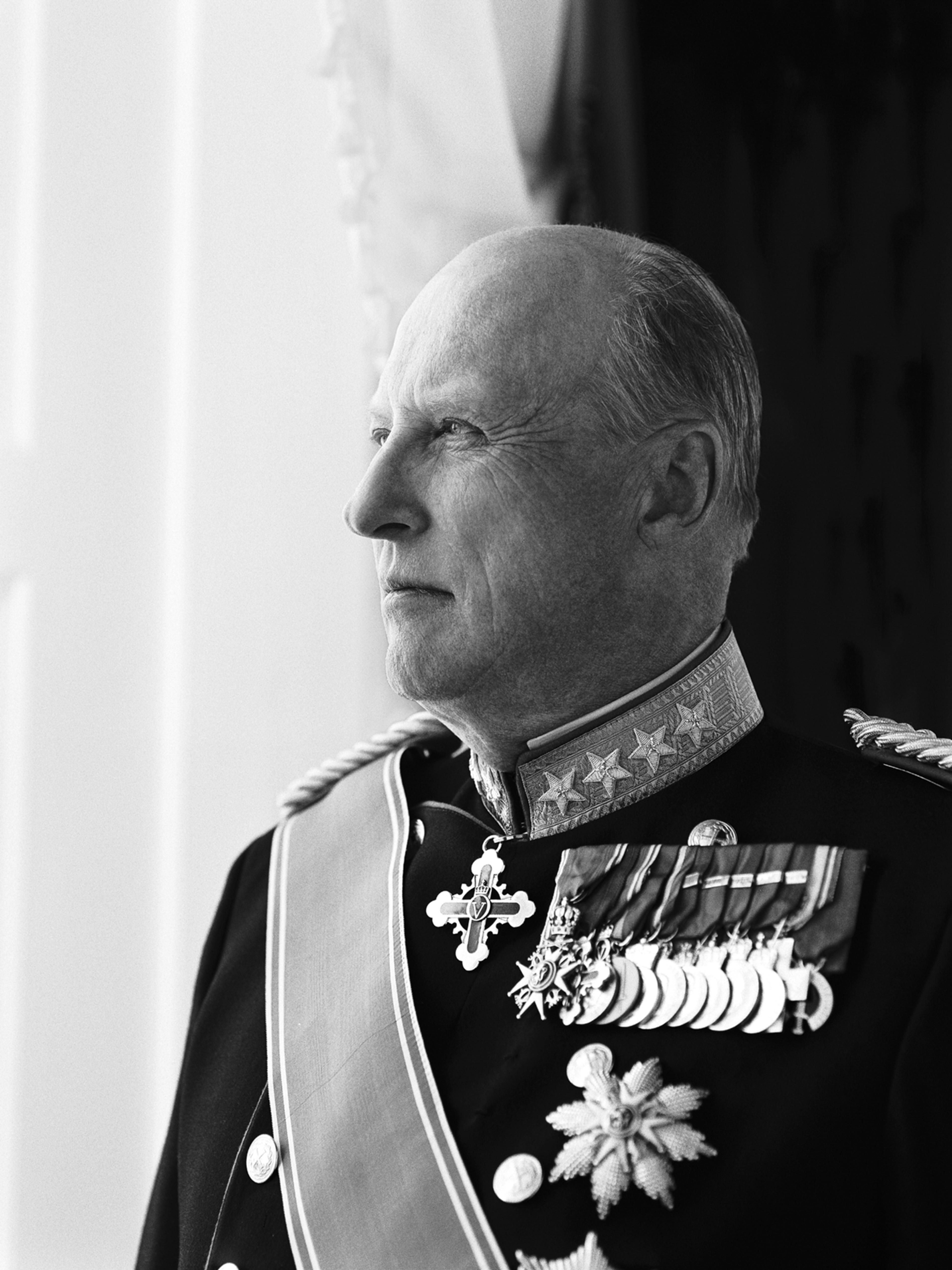 Sort hvitt portrett av Kong Harald, i gallauniform - ser ut av vinduet.