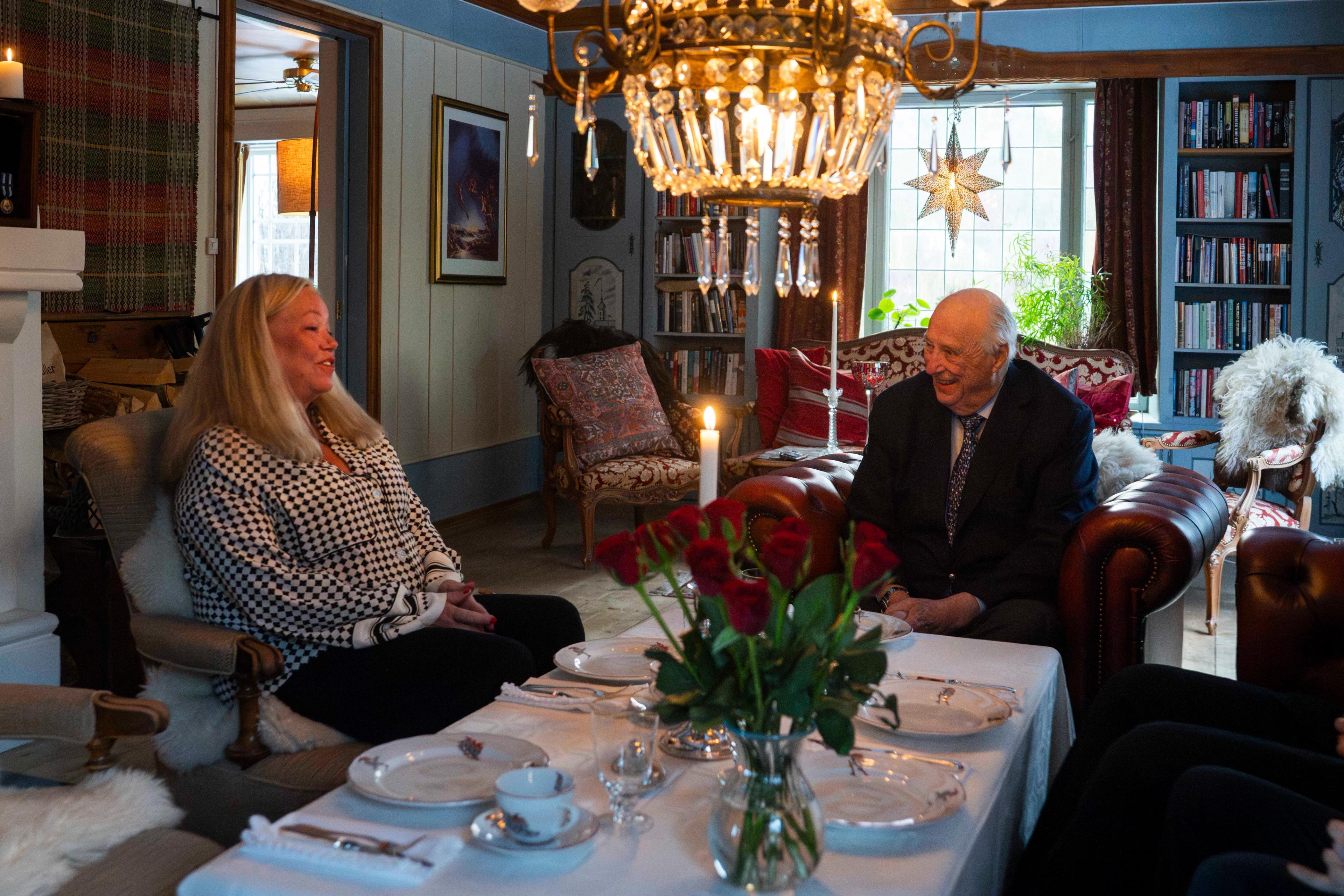 Kong Harald sitter ved et oppdekket bord sammen med Bjørg. Hjemmekoselig stue.
