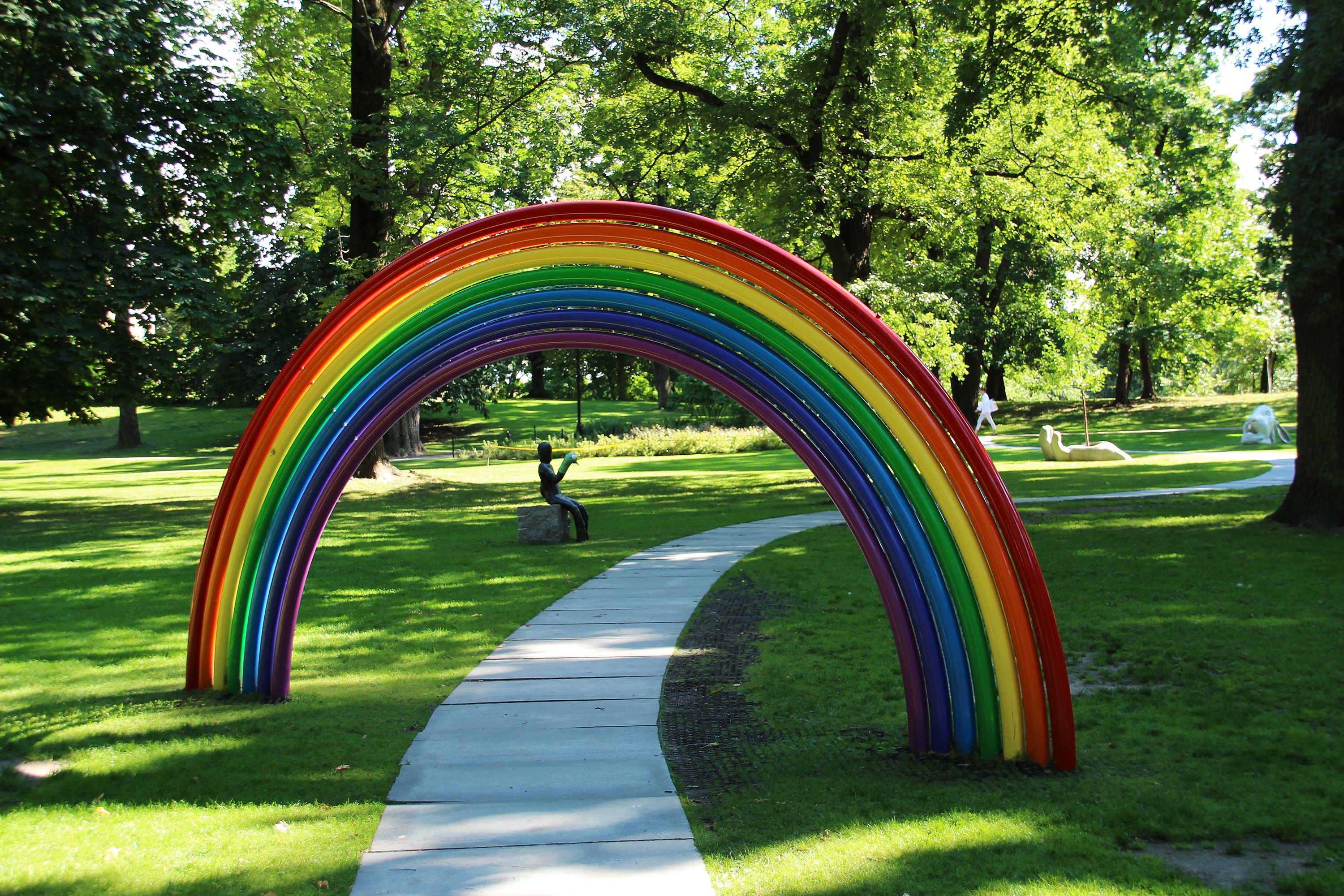 En hellelagt sti slynger seg under en fargerik regnbue. Lenger ned langs stien skimtes flere skulpturer