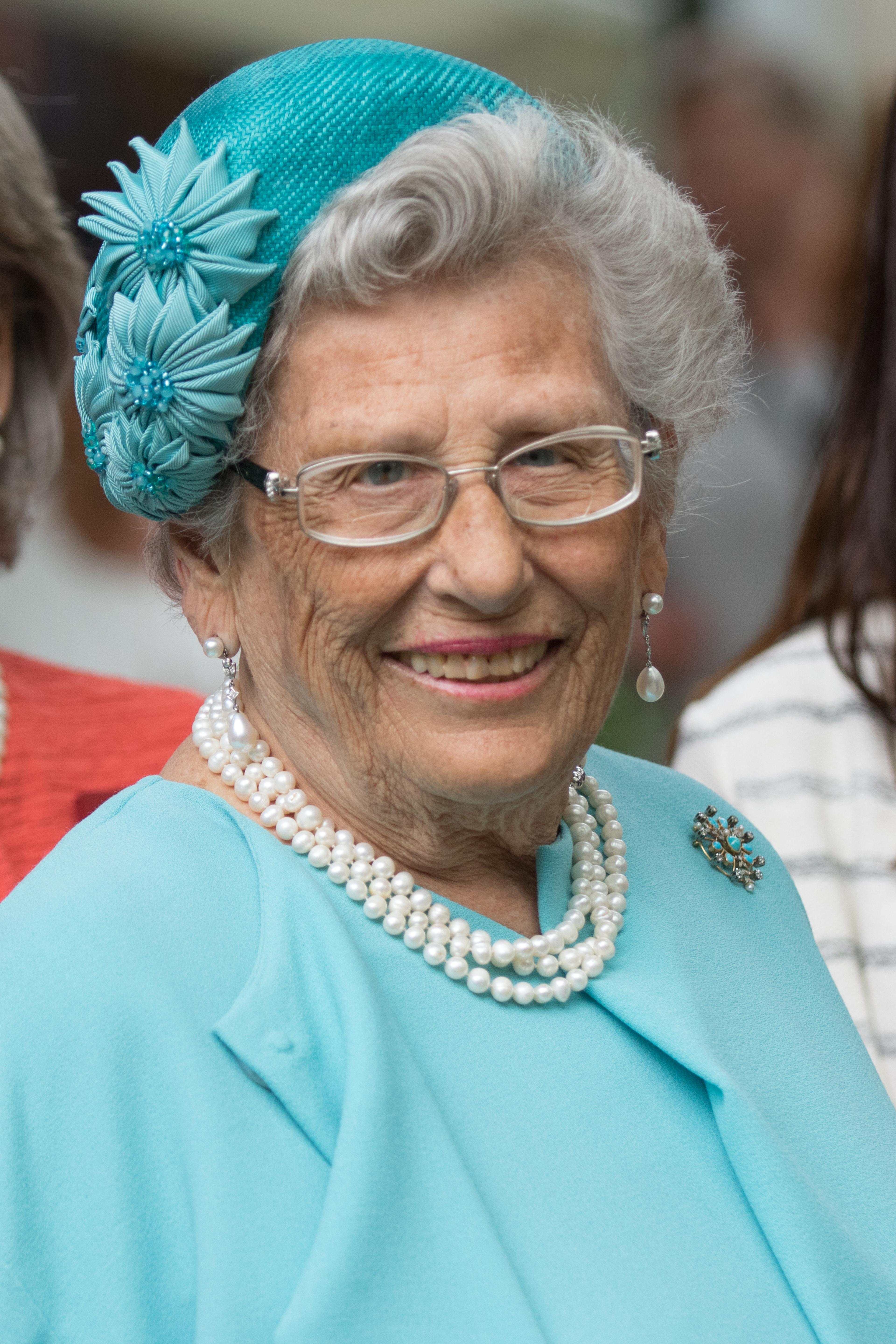 Portrettbilde av em smilende Prinsesse Astrid i turkis drakt, matchende hatt, perlekjede og perleøredobber.