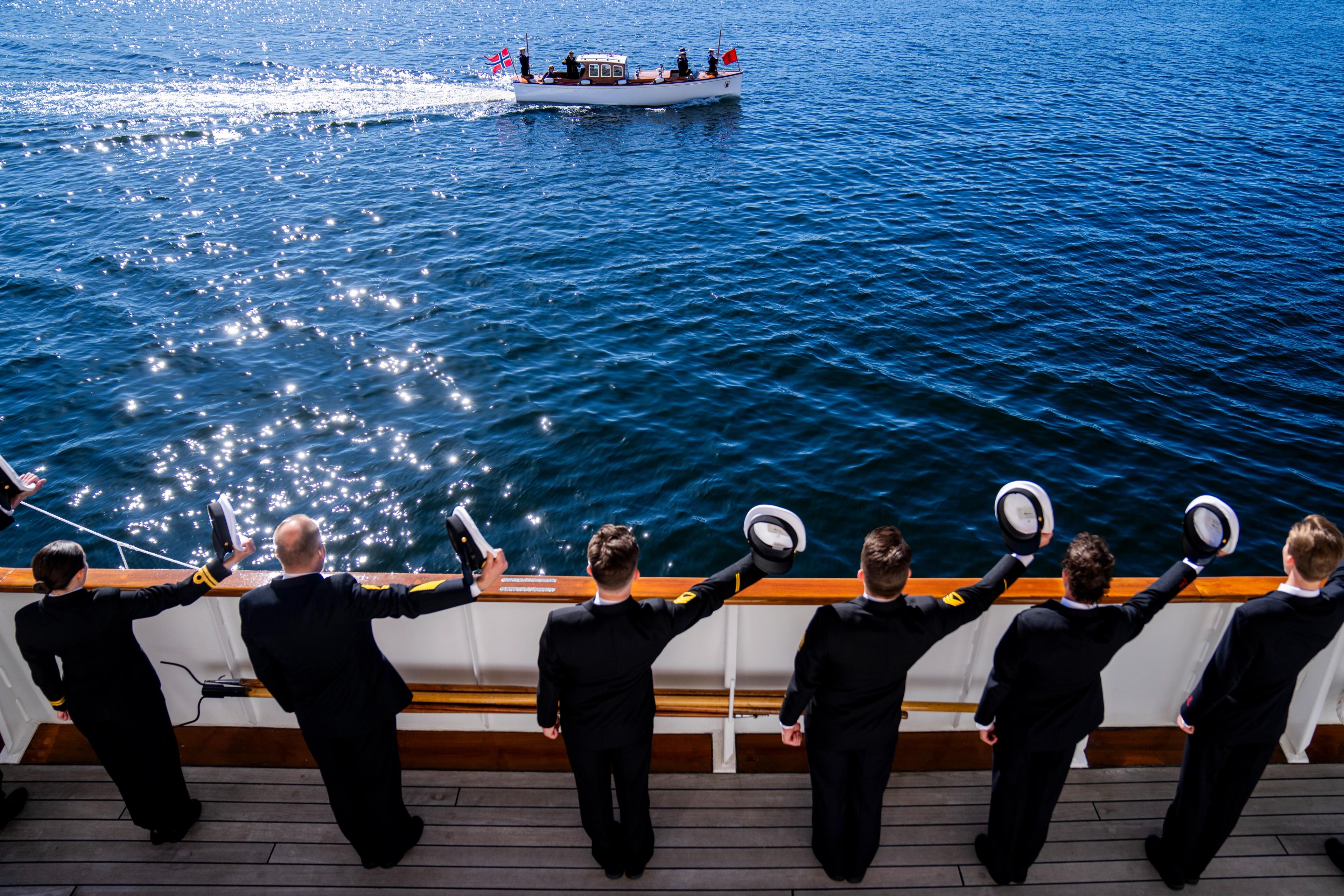 Befalet står på rekke på dekk og helsar med luene, medan sjaluppen passerer.