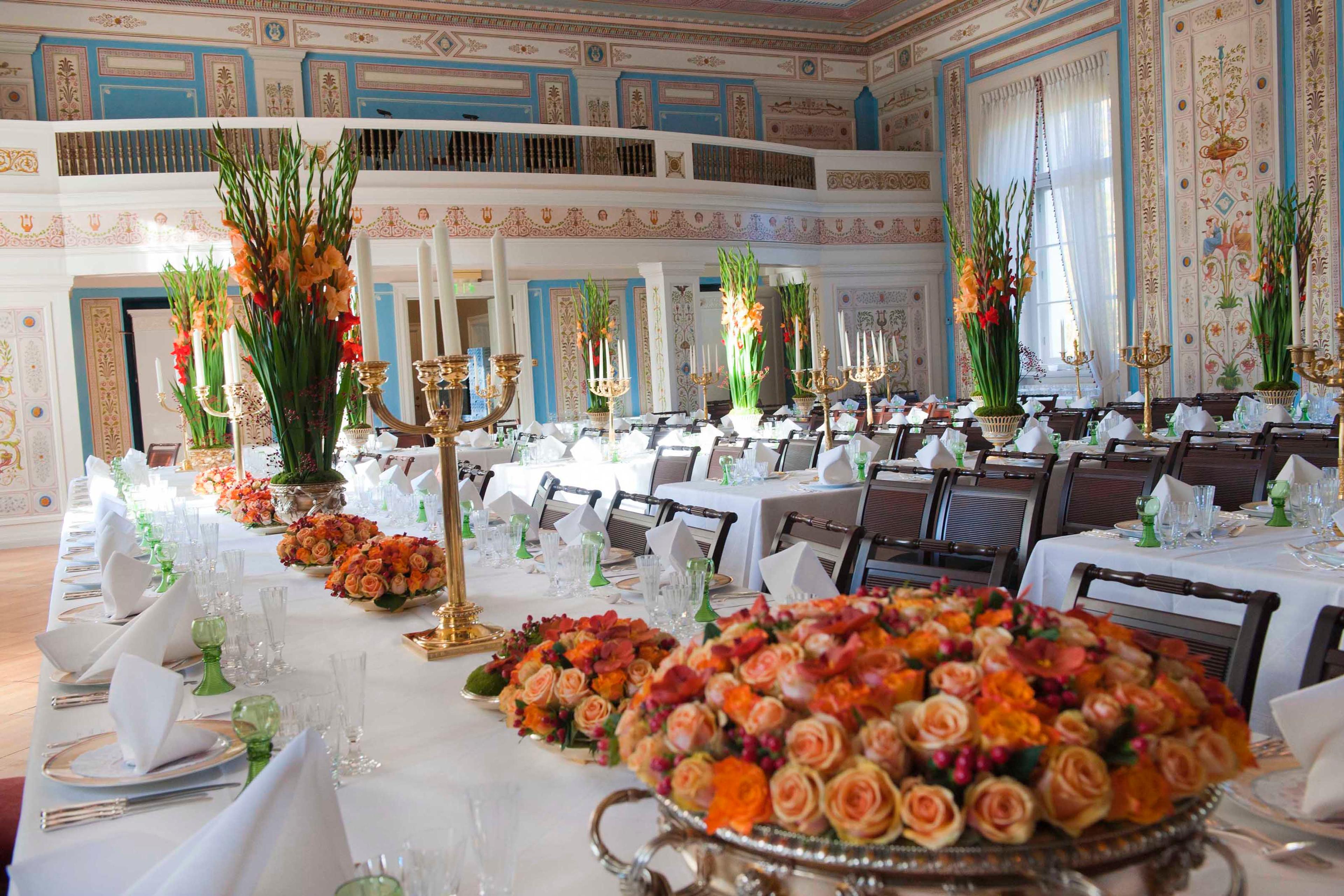 Bordene dekket med hvite duker, servise, og blomsteroppsatser i oransjetoner.