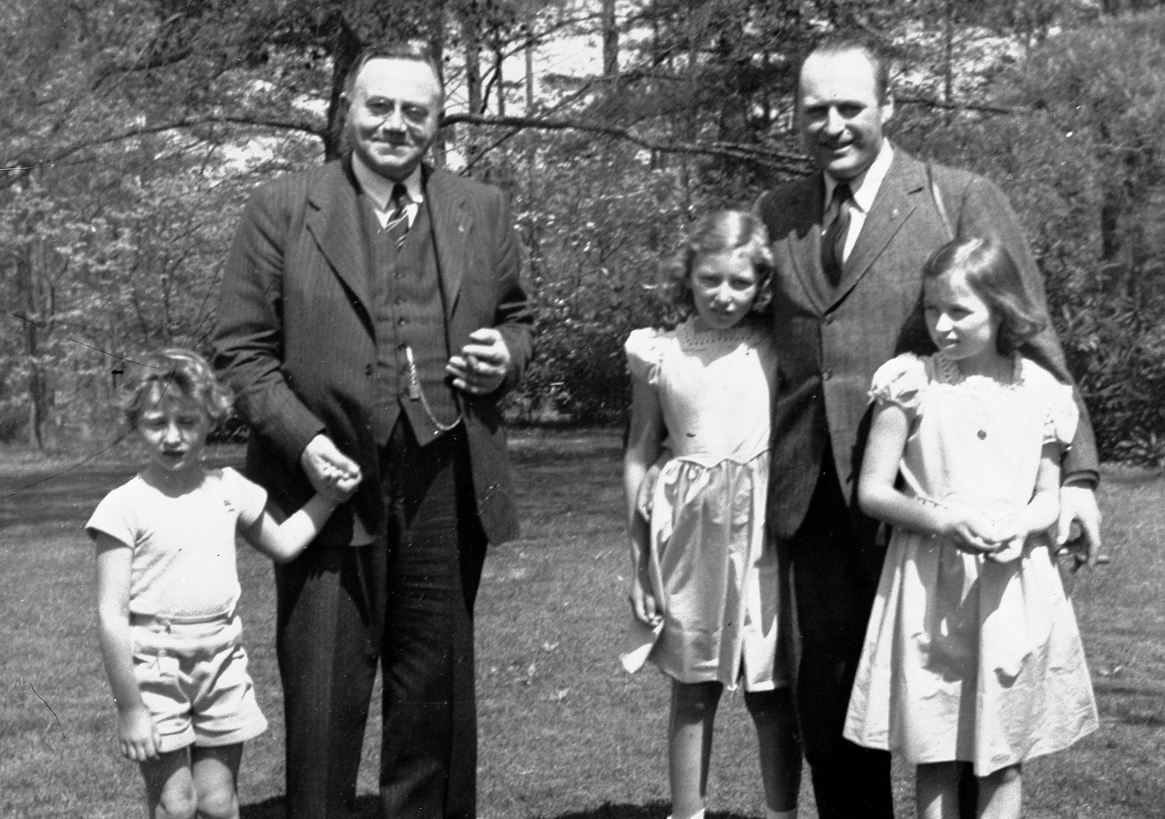 Statsministeren og Kronprins Olav står ute i hagen med Prins Harald, Prinsesse Astrid og Prinsesse Ragnhild foran seg.