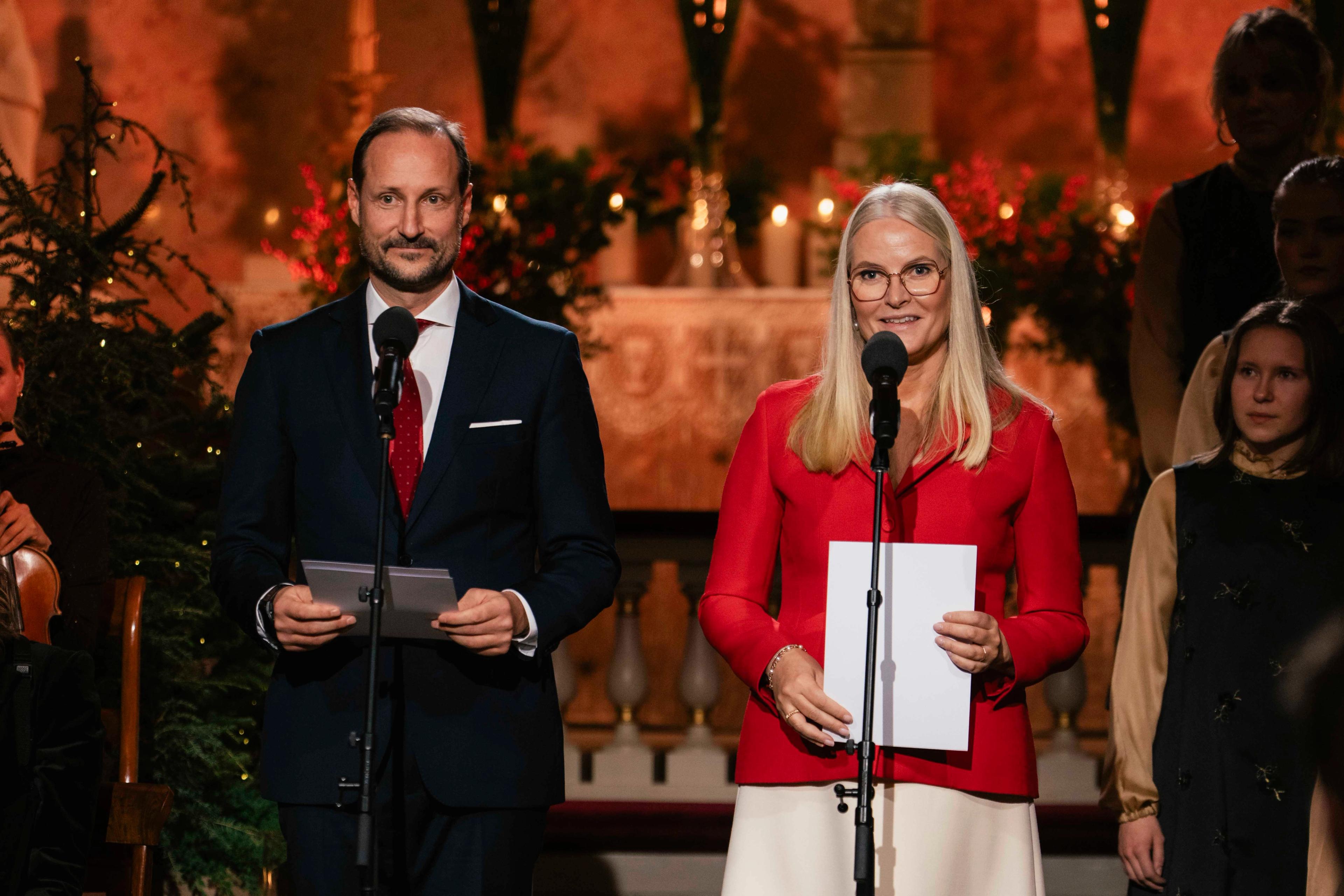 Kronprins Haakon og Kronprinsesse Mette-Marit står foran hver sin stående mikrofon med et julepyntet alter i bakgrunnen.