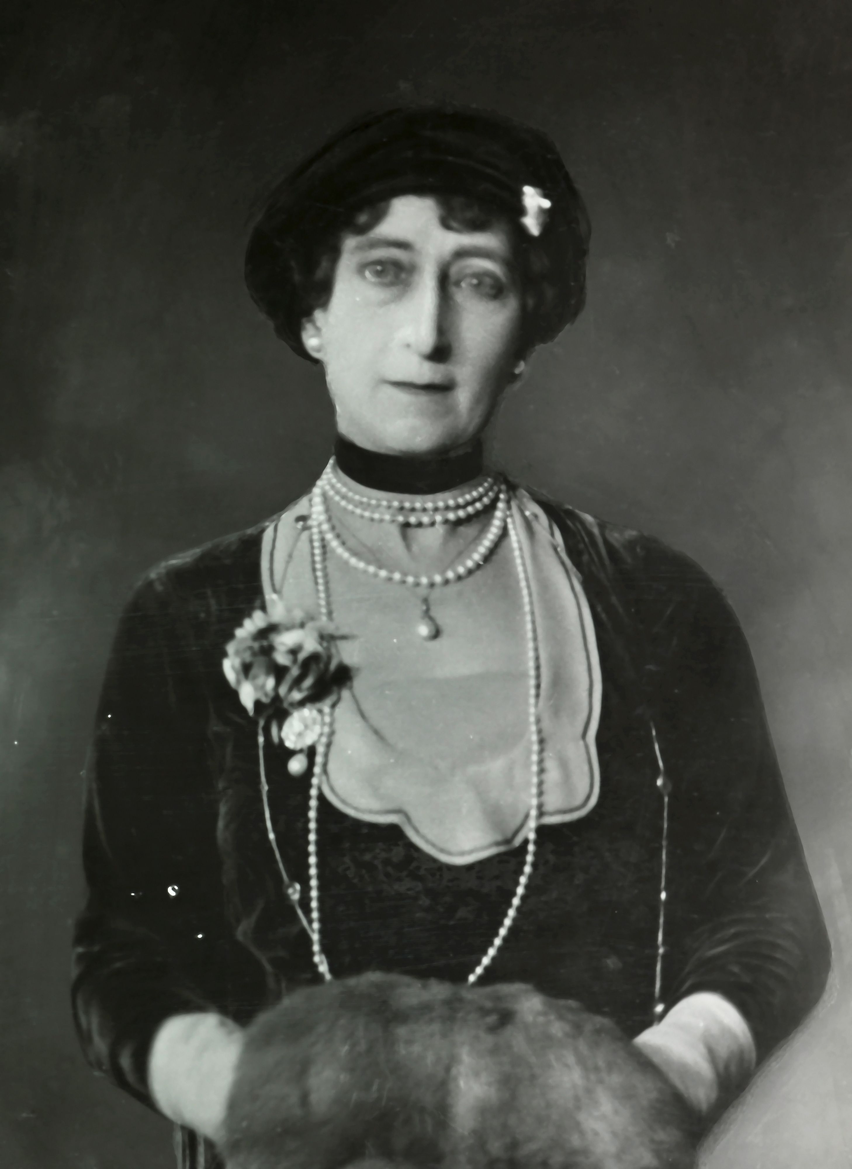 Portrett av Dronning Maud med langt perlekjede og muffe i skinn.