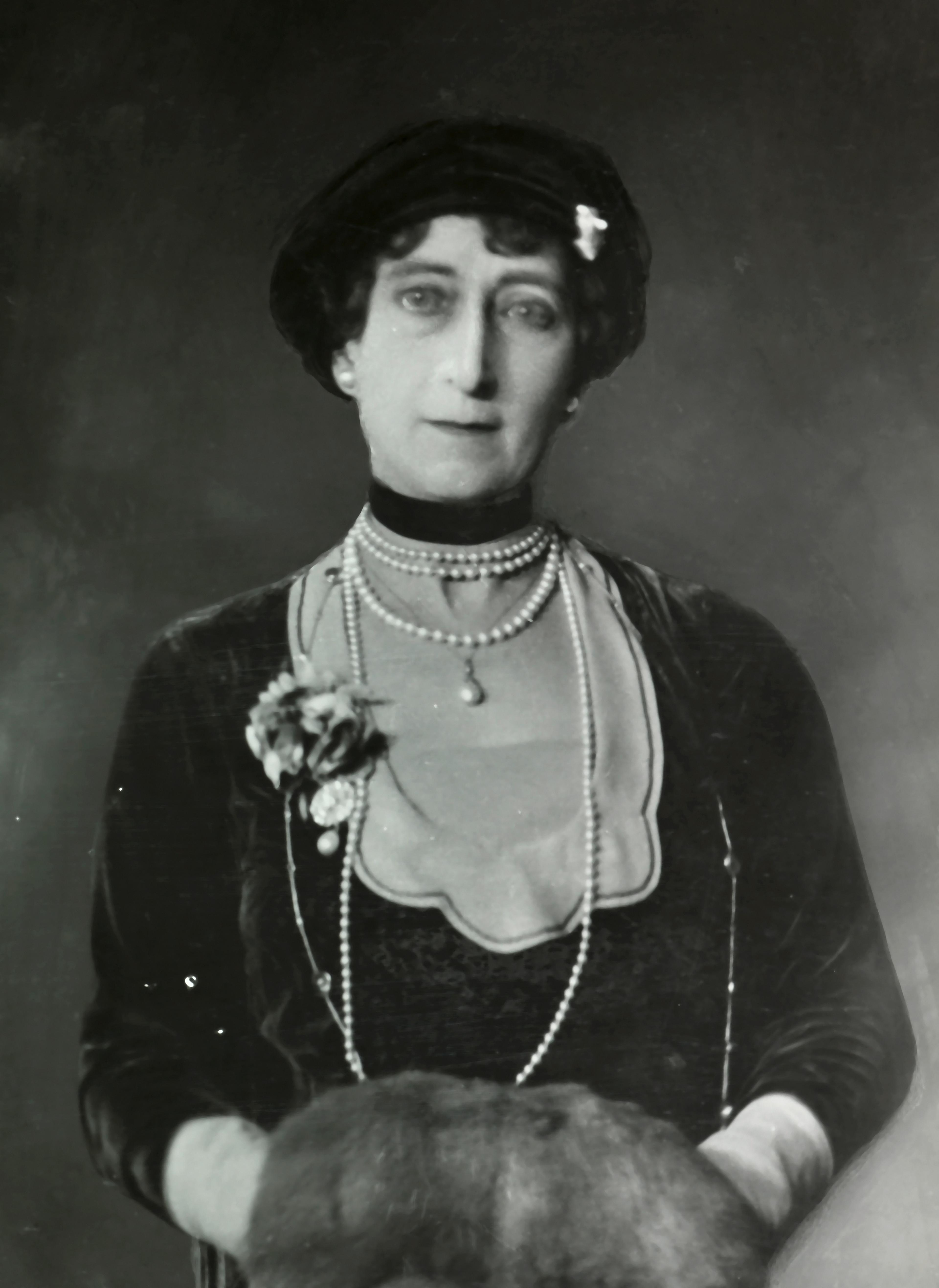 Portrett av Dronning Maud med langt perlekjede og muffe i skinn.