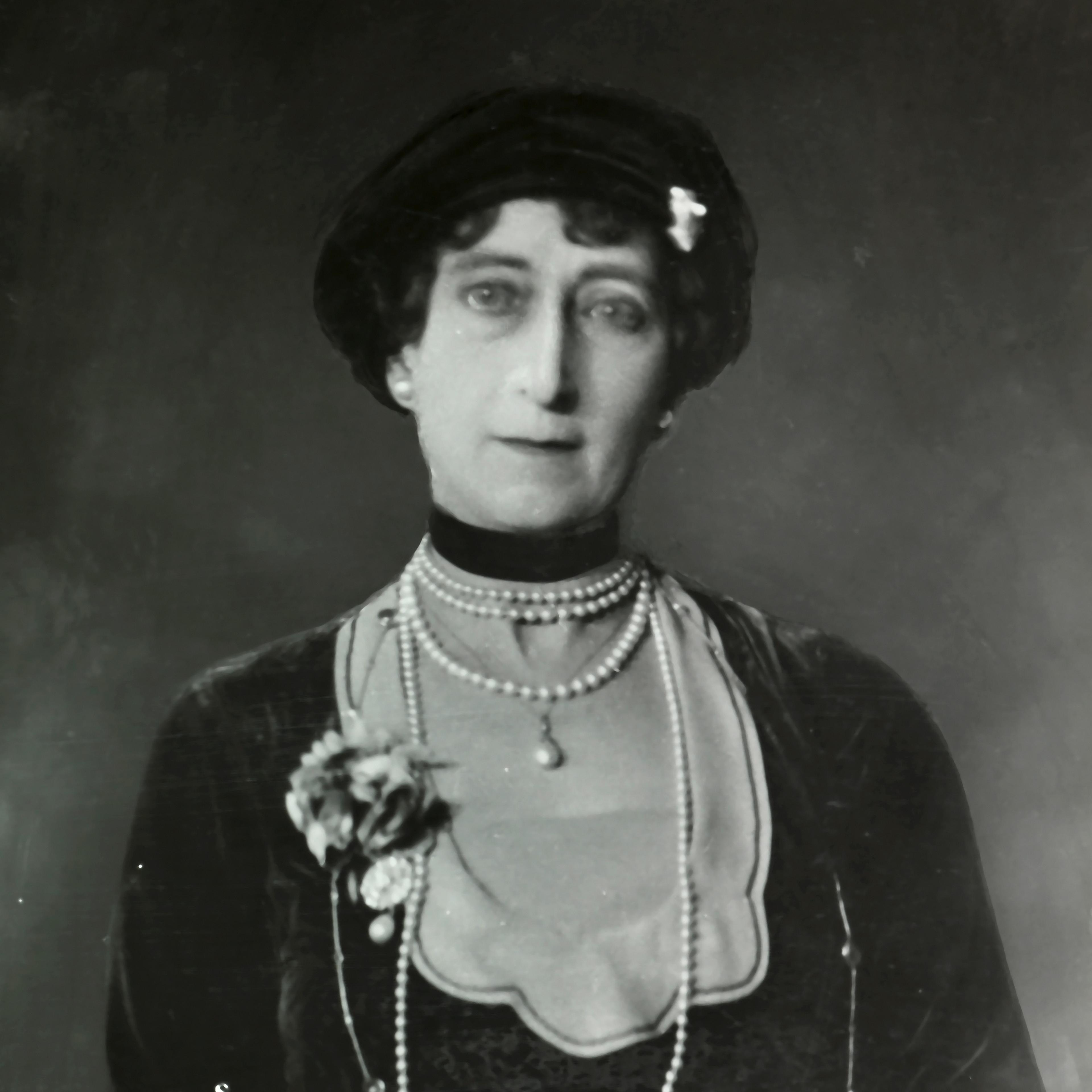 Portrett av Dronning Maud med langt perlekjede og muffe i skinn.