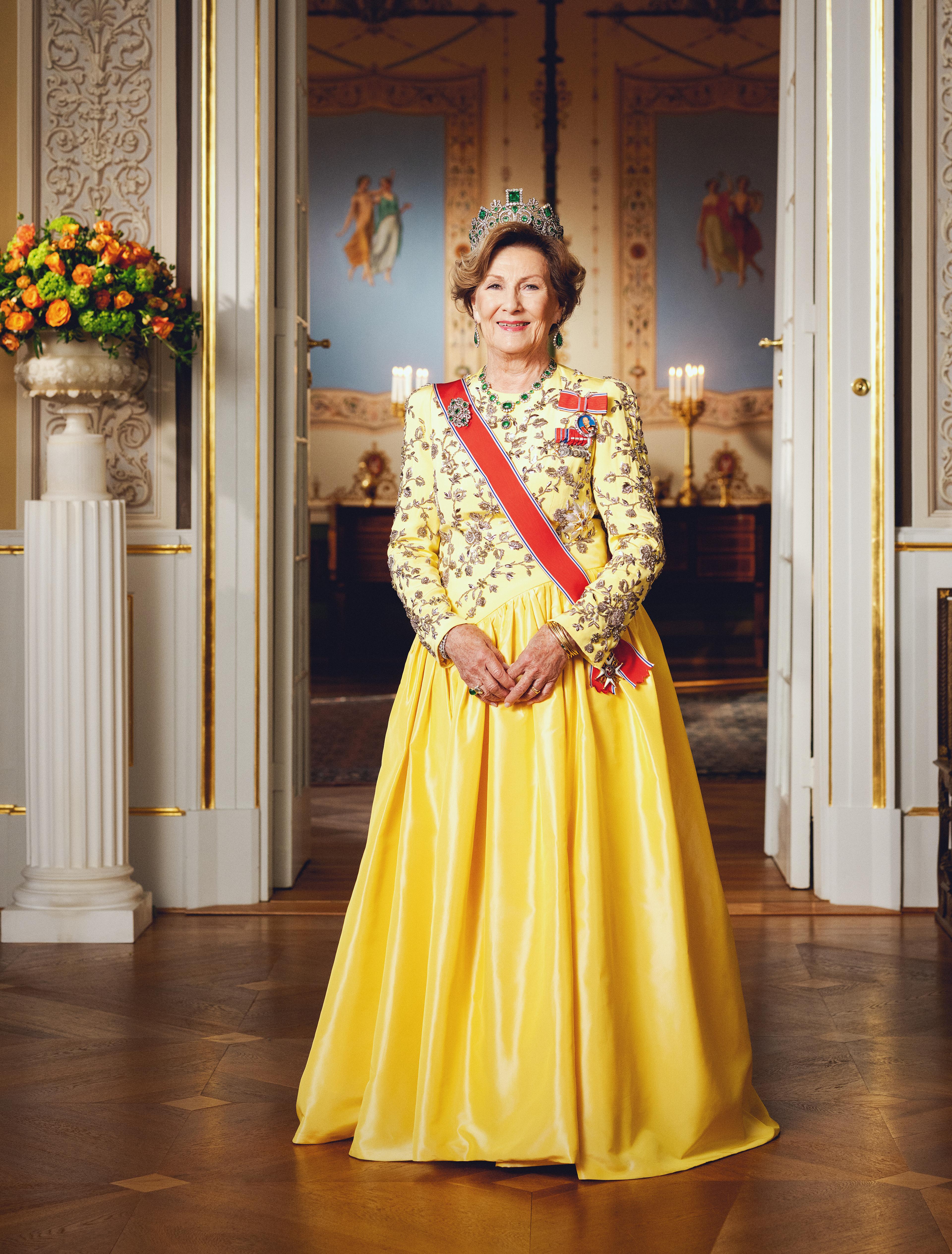Dronning Sonja står i gul gallakjole med ordener og diadem.