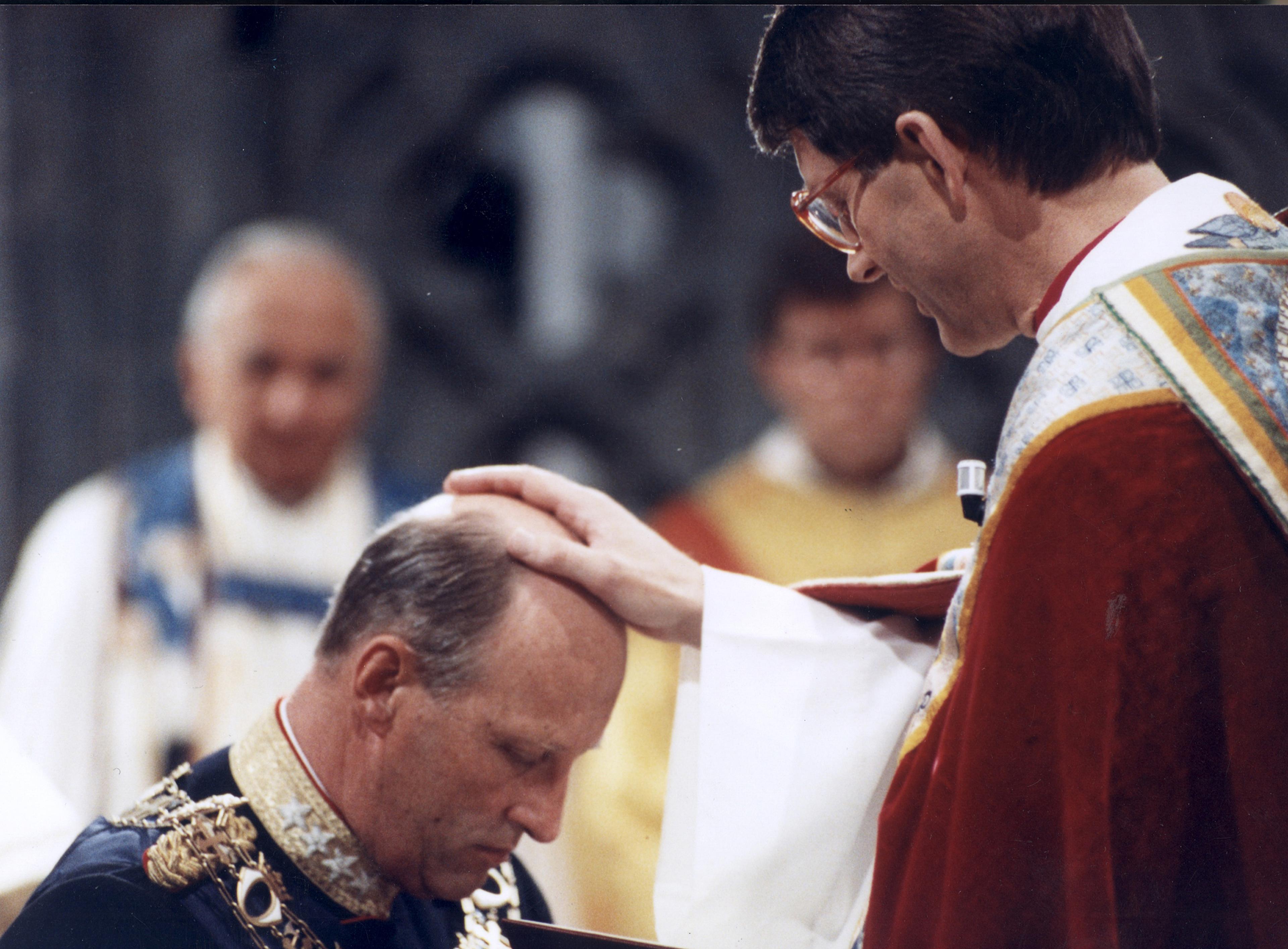 Kongen kneler foran biskopen, som har hånden på Kongens hode.