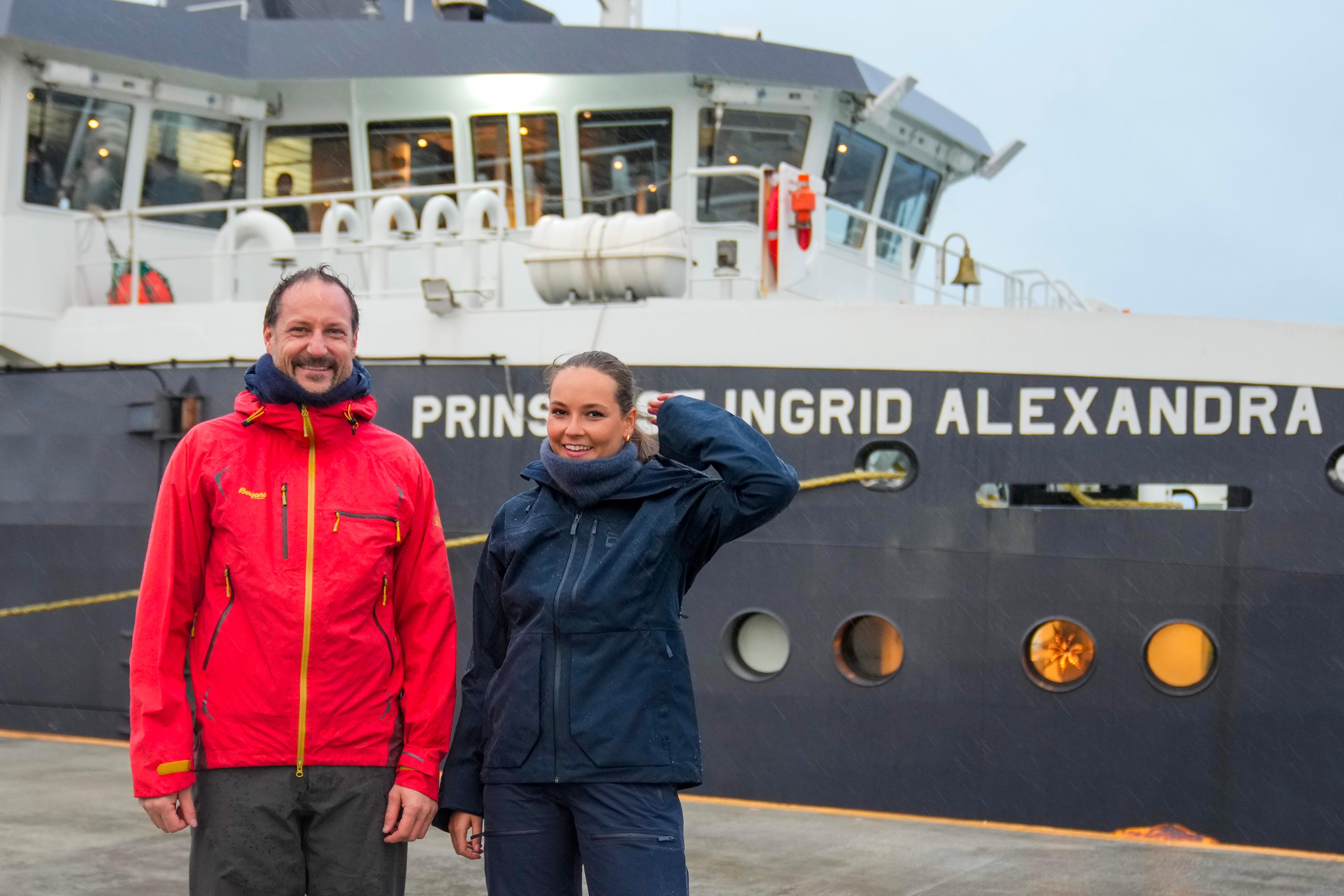 Kronprins Haakon og Prinsesse Ingrid Alexandra i regntøy på kaia foran skipet, som har Prinsessens navn i baugen.