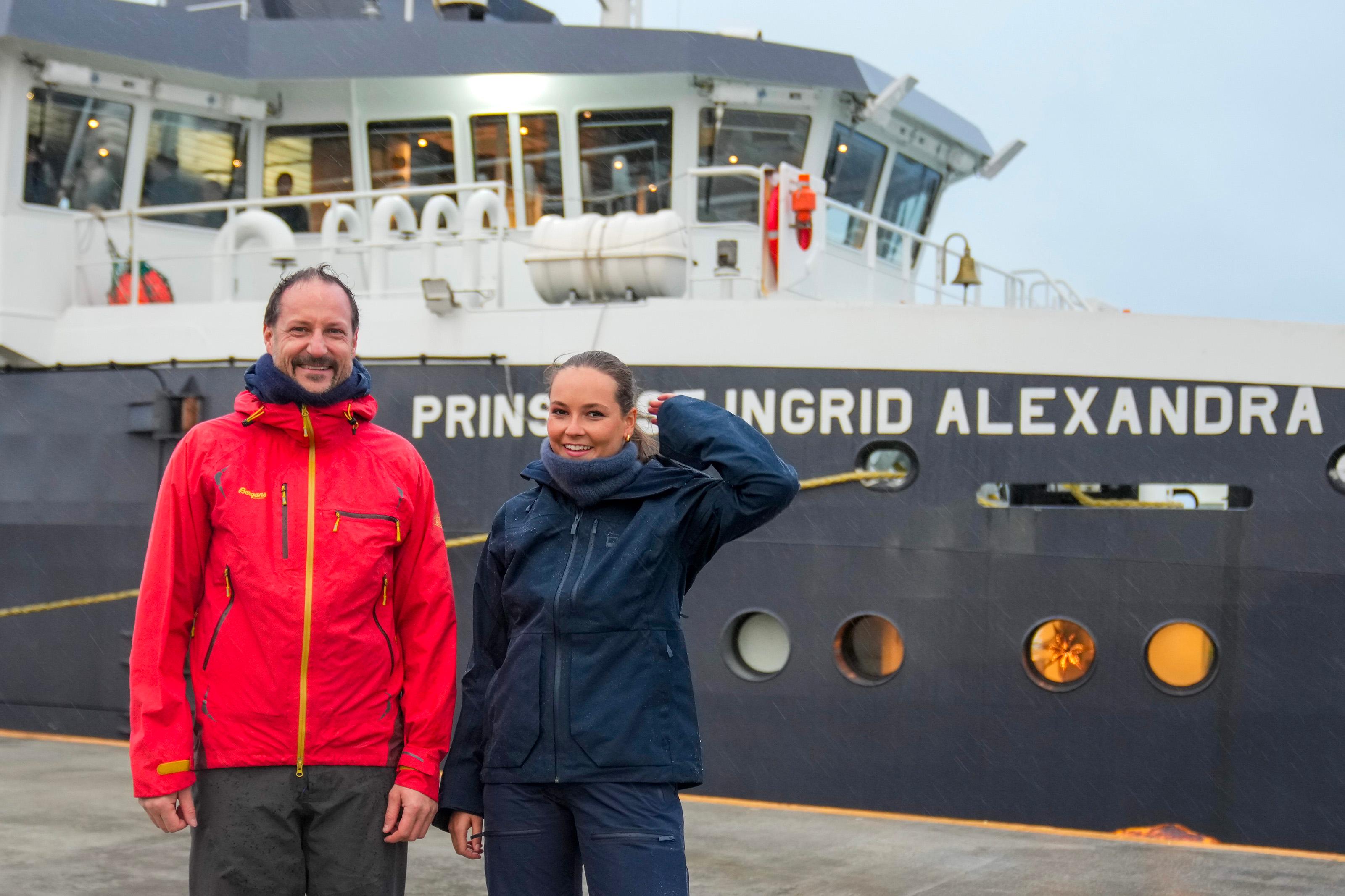 Kronprins Haakon og Prinsesse Ingrid Alexandra i regntøy på kaia foran skipet, som har Prinsessens navn i baugen.