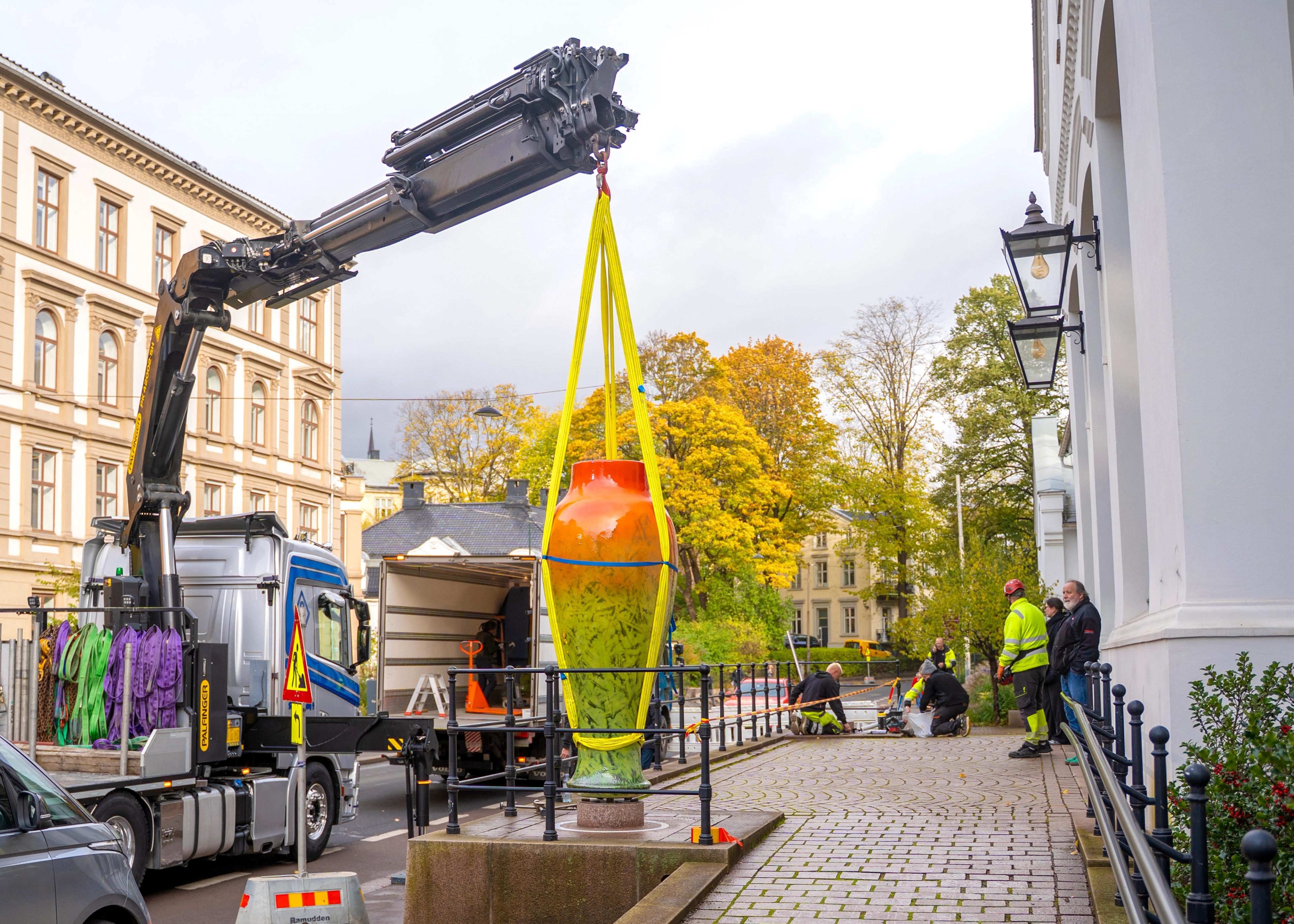 En stor krukke i orange og gule toner løftes med kranbil for å plasseres utenfor KunstStallen.