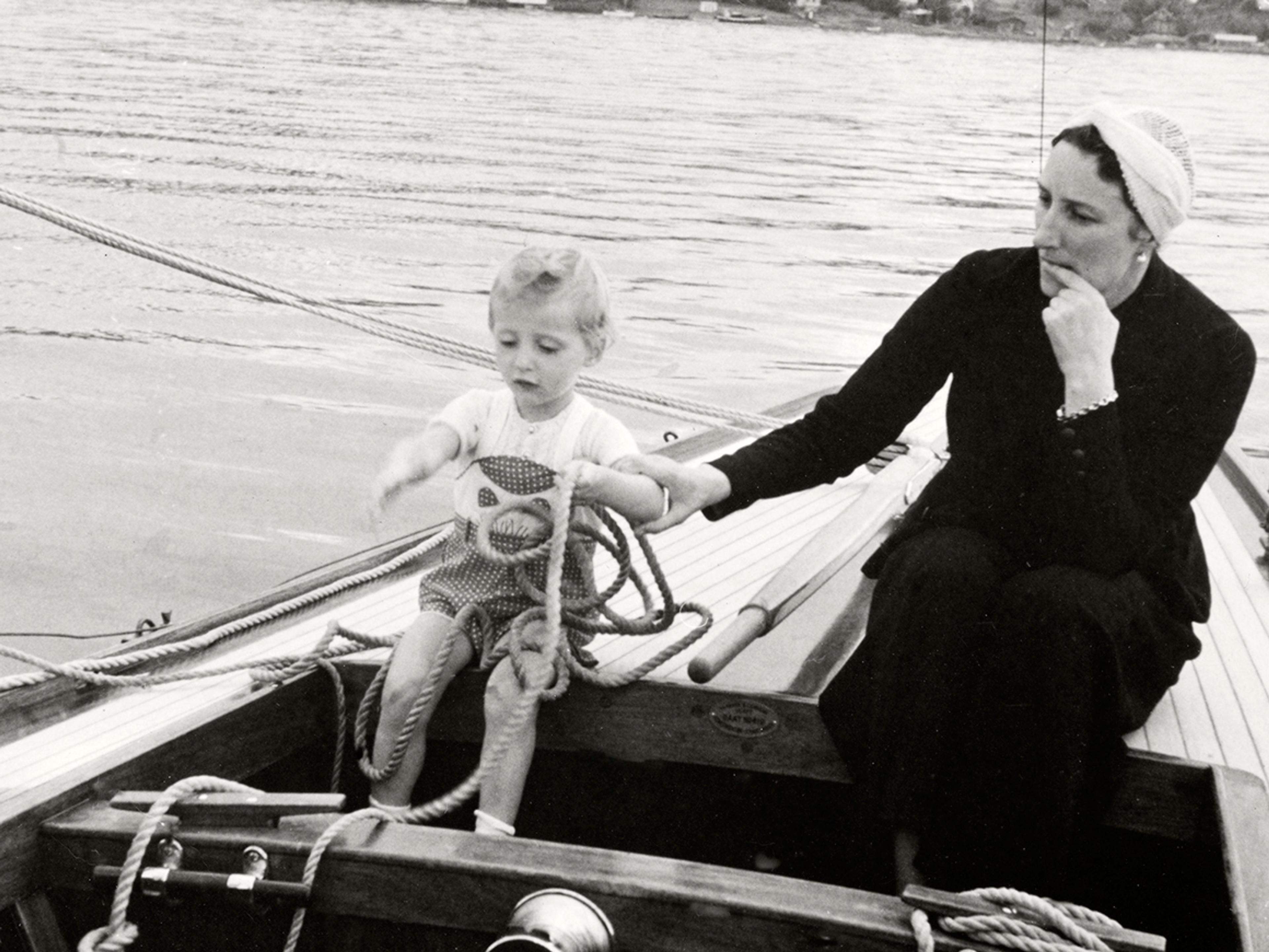 Kronprinsesse Märtha og Prins Harald sitter akterut i en seilbåt. Kronprinsessen ser litt betenkt på Prinsen, som er opptatt med tauverk.