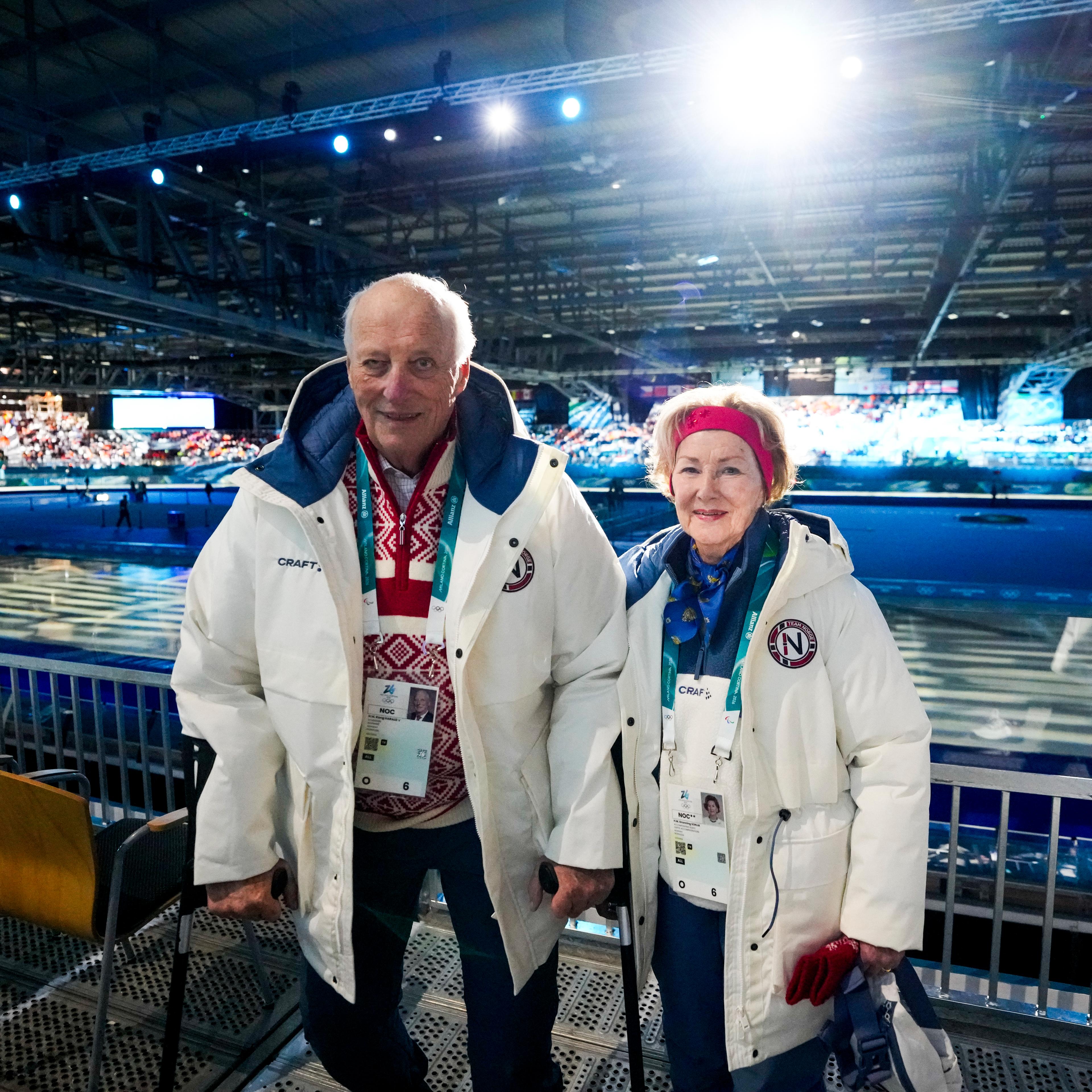Kongeparet iført OL-antrekk med skøytestadio i bakgrunnen.