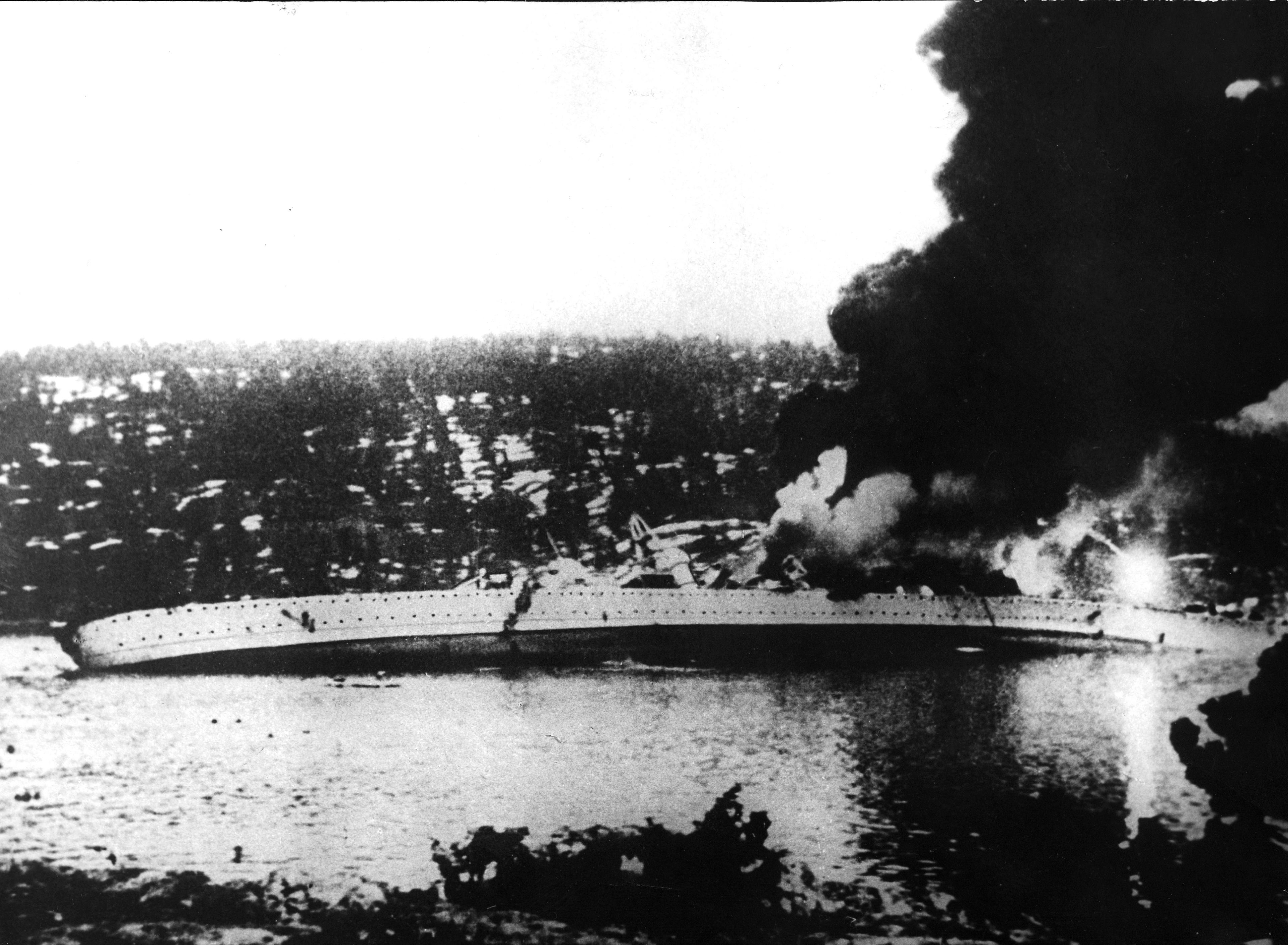 Slagskipet ligger over på siden og det brenner om bord.