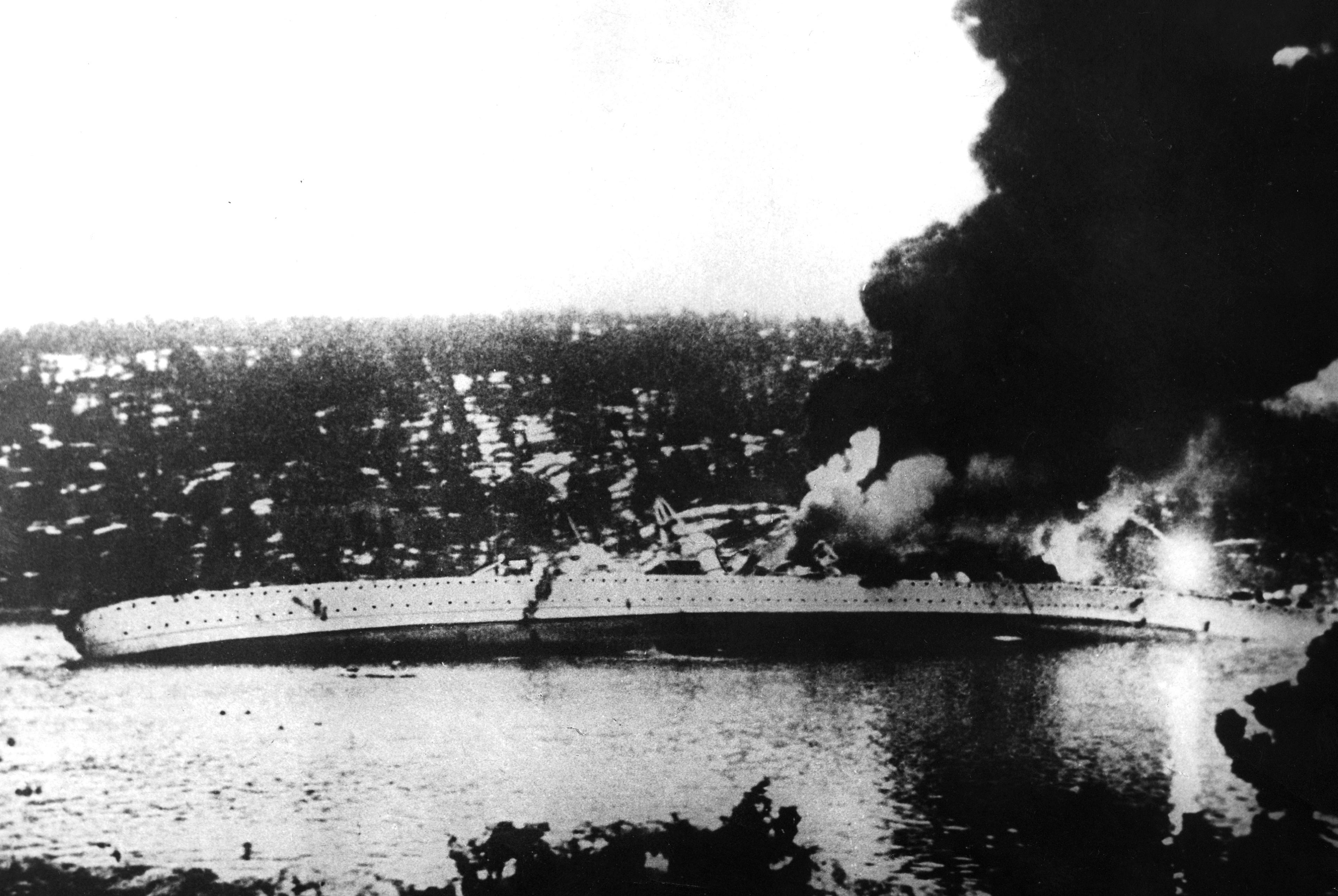 Slagskipet ligger over på siden og det brenner om bord.