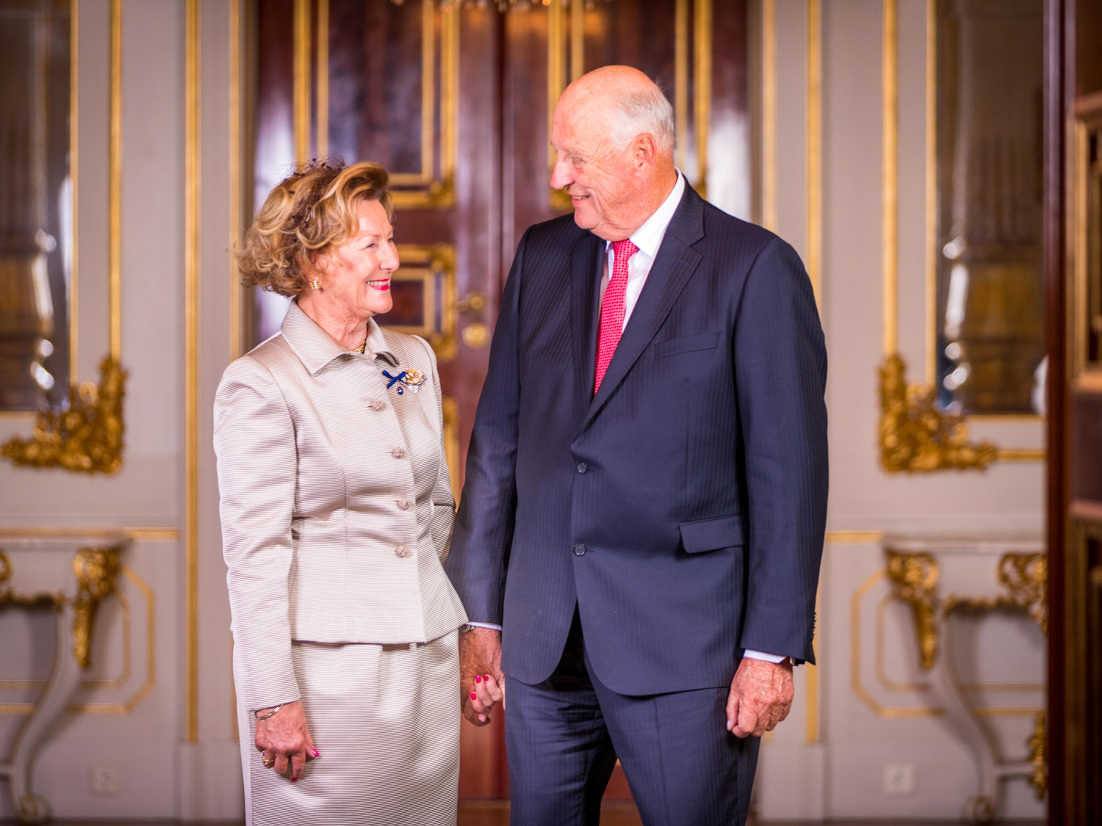 Kongen og Dronningen ser smilende på hverandre. Holder hverandre i hånden.