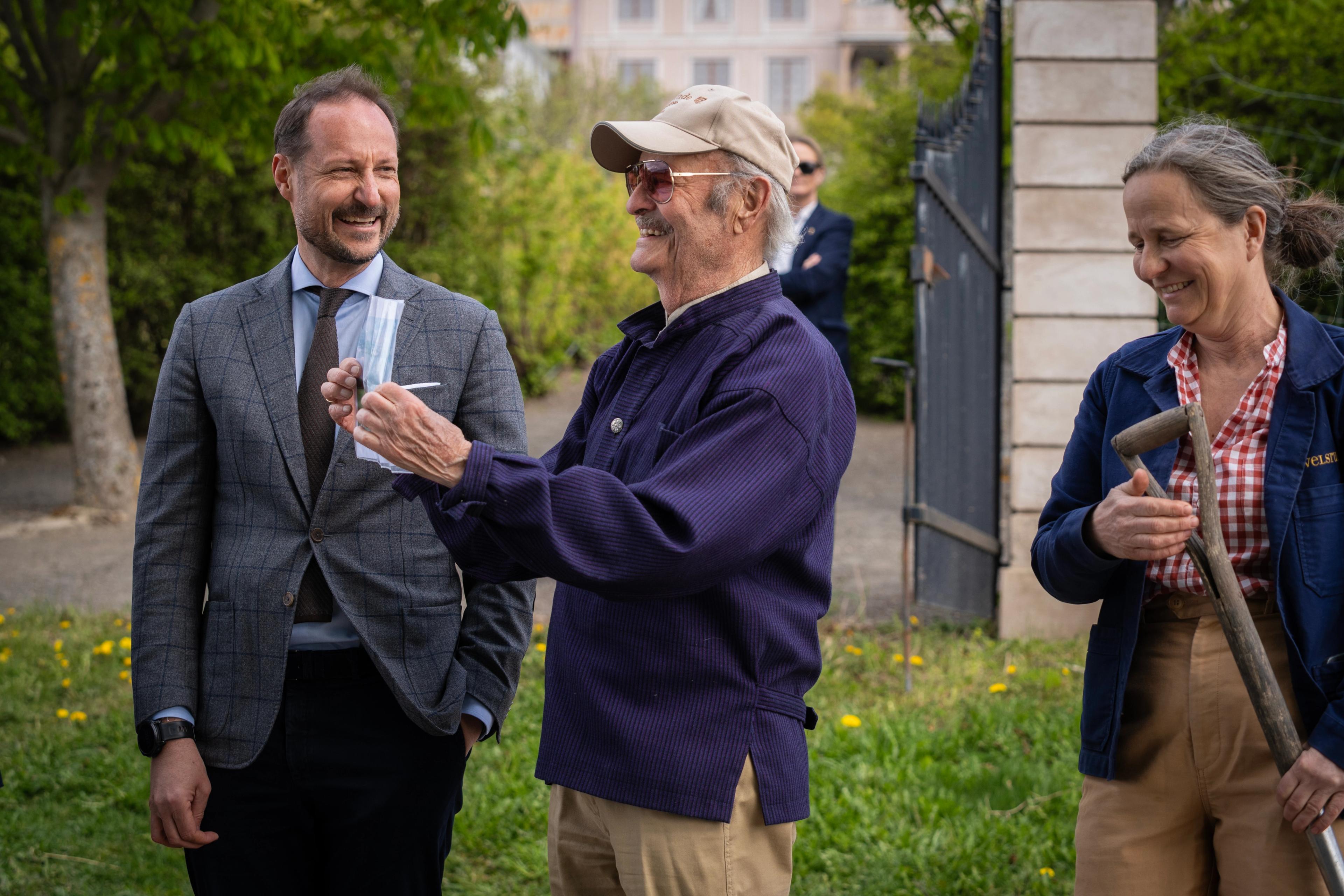 Kronprins Haakon, far og datter smiler mens Wilhelm Olssøn viser fram bildet.