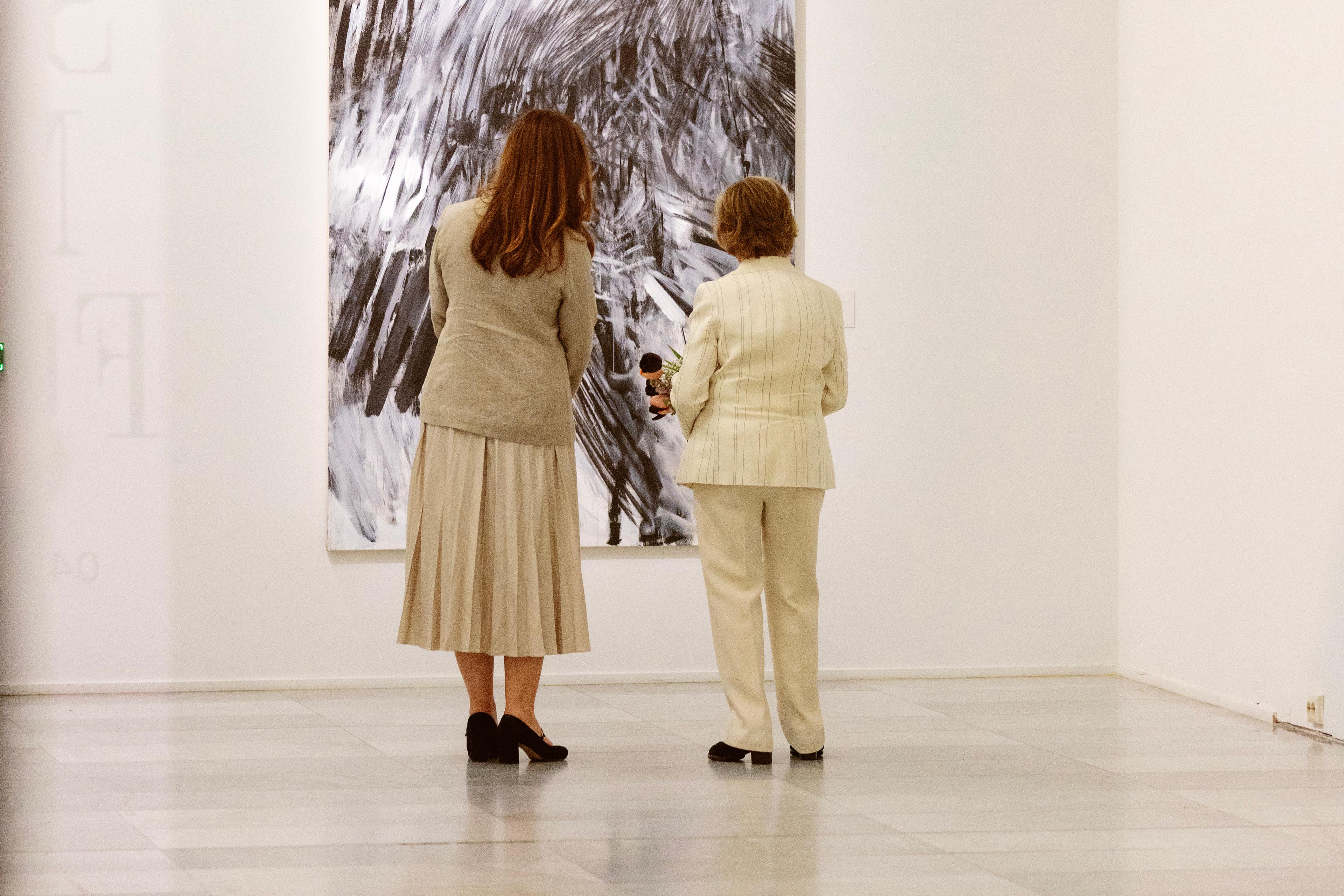 Dronning Sonja og Ingrid betrakter et verk. Vi ser dem bakfra.