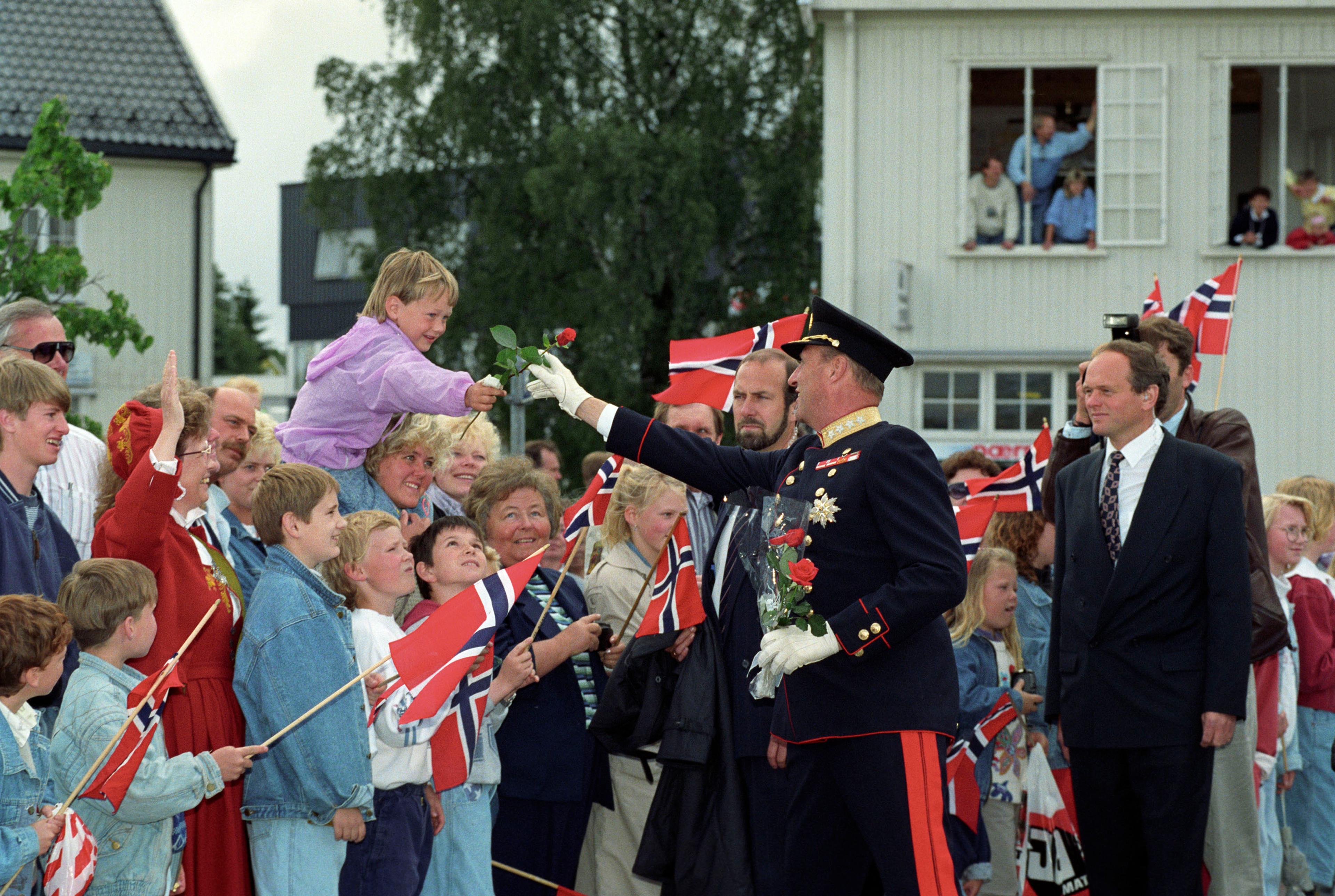 Kong Harald får en rose av en liten gutt som sitter på skuldrene til foreldrene.