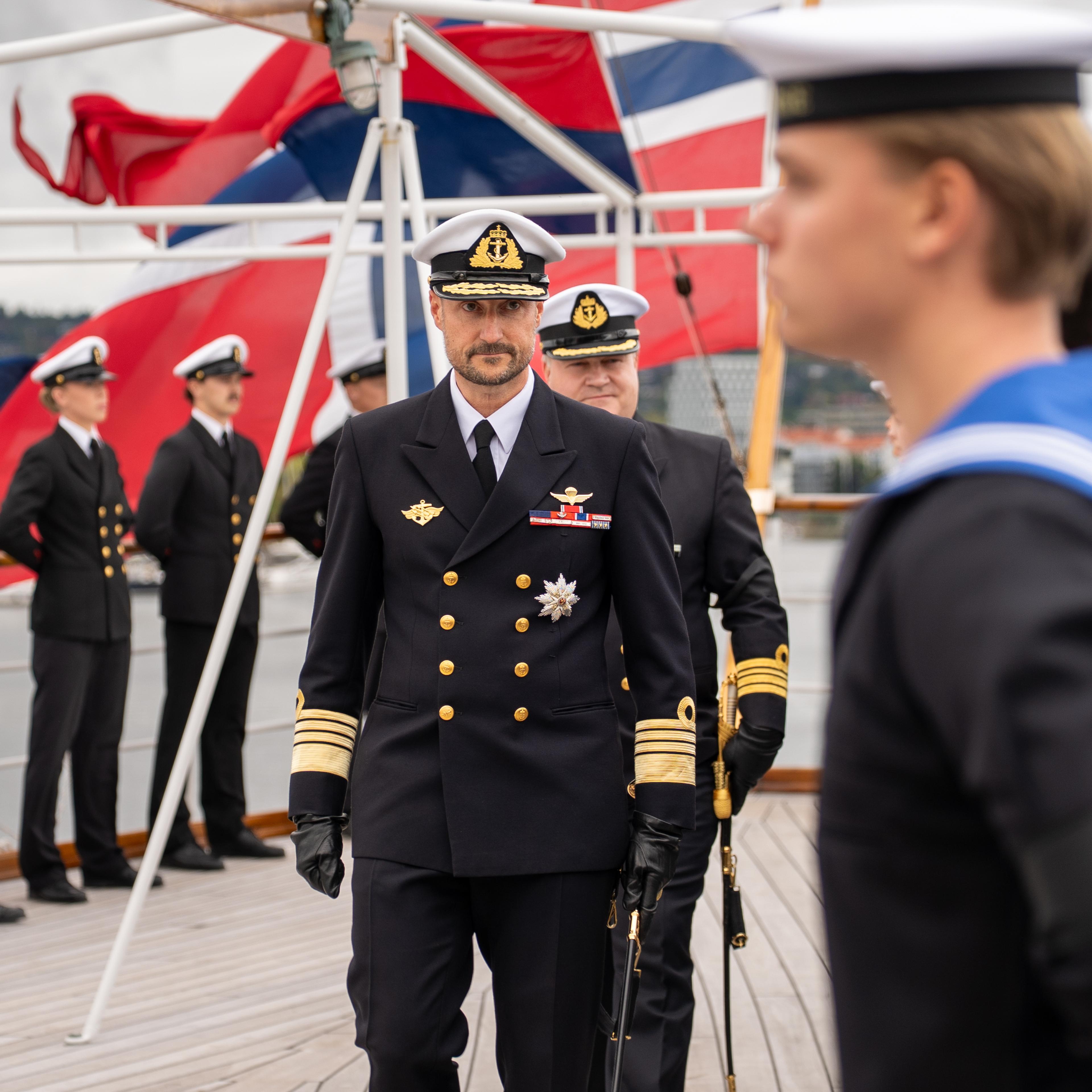 Kong Haakon passerer ei rekkje vernepliktige, medan skipssjefen går bak.