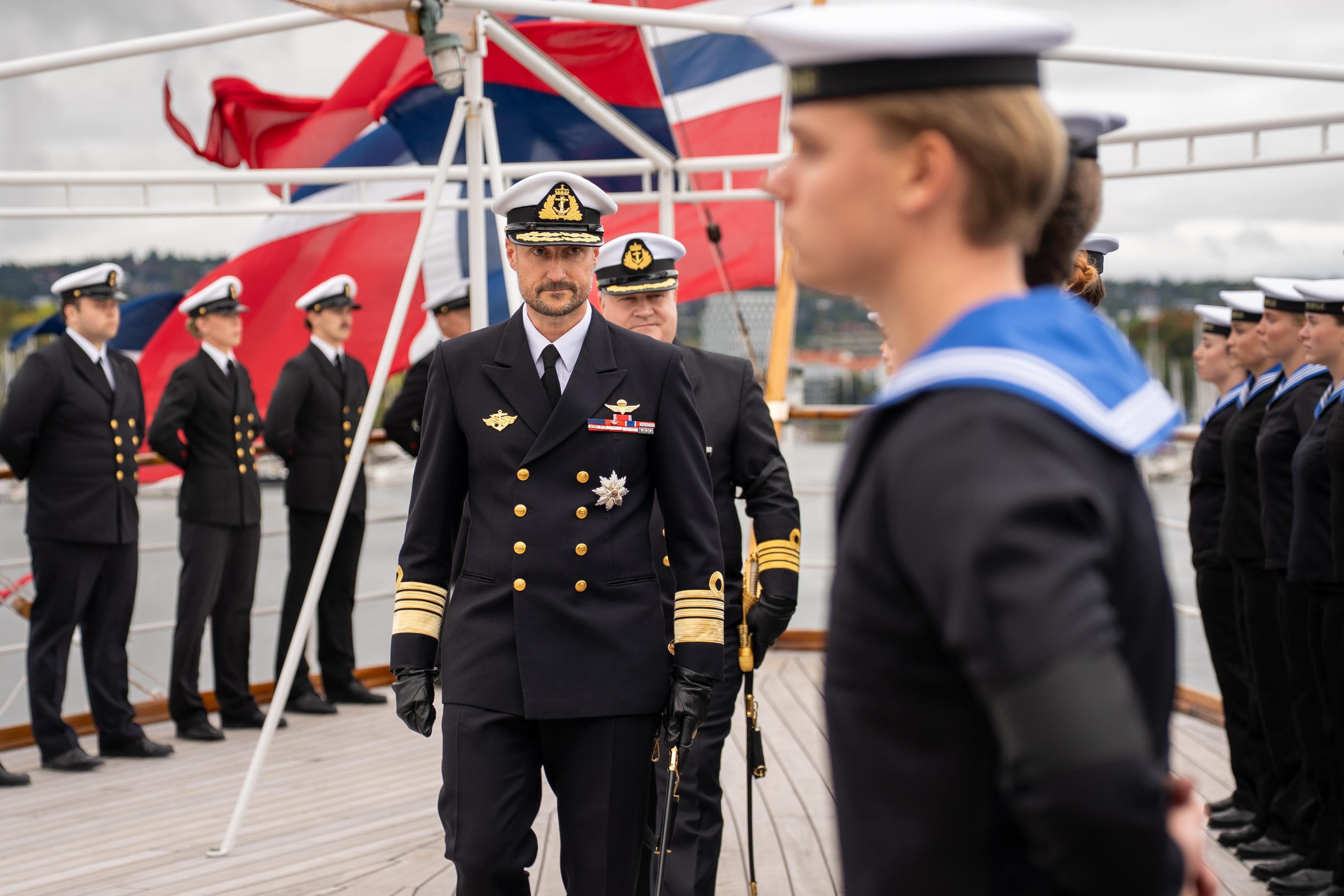 Kong Haakon passerer ei rekkje vernepliktige, medan skipssjefen går bak.