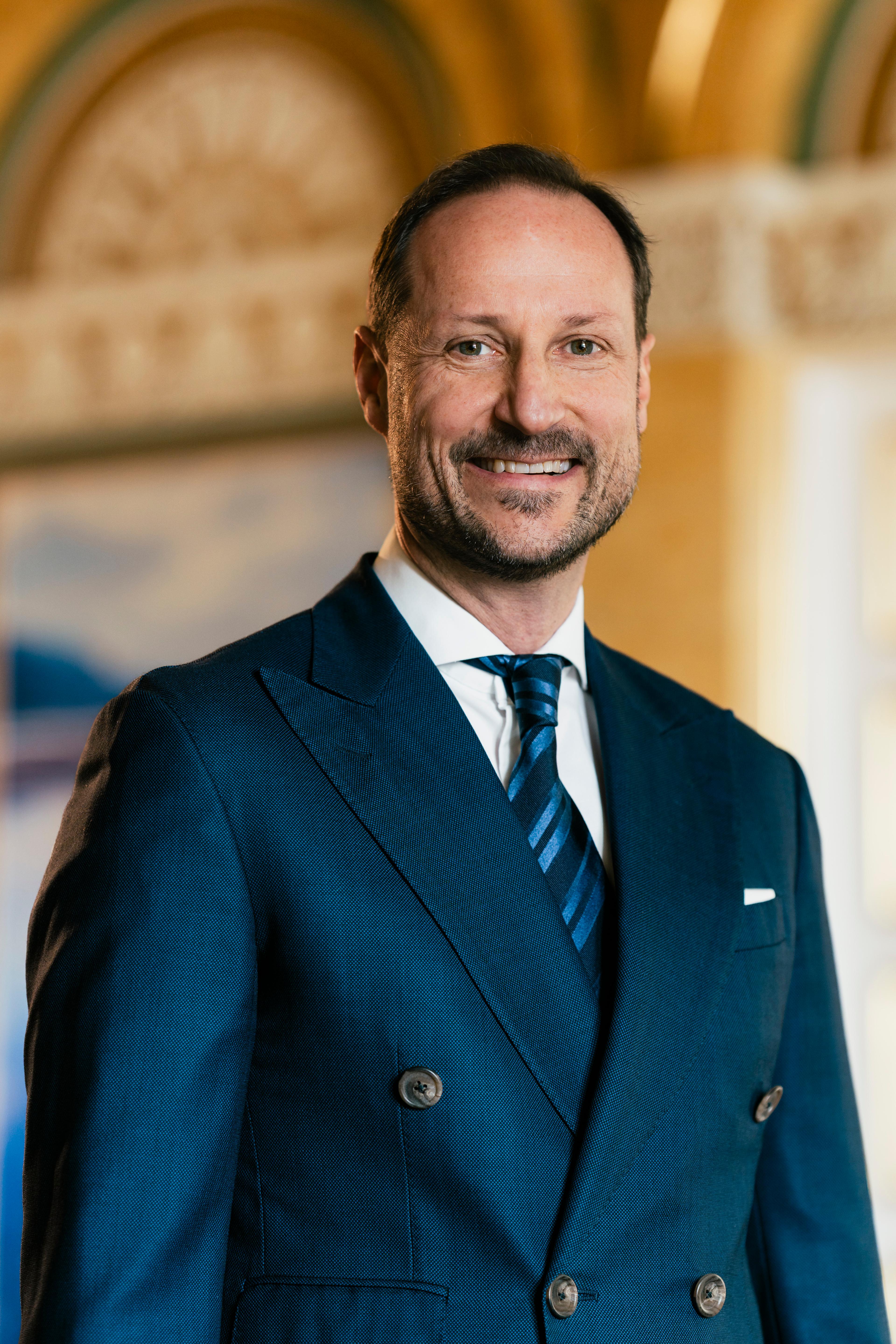 Portrett av Kronprins Haakon tatt i hvit skjorte mørkeblå dress med slips.