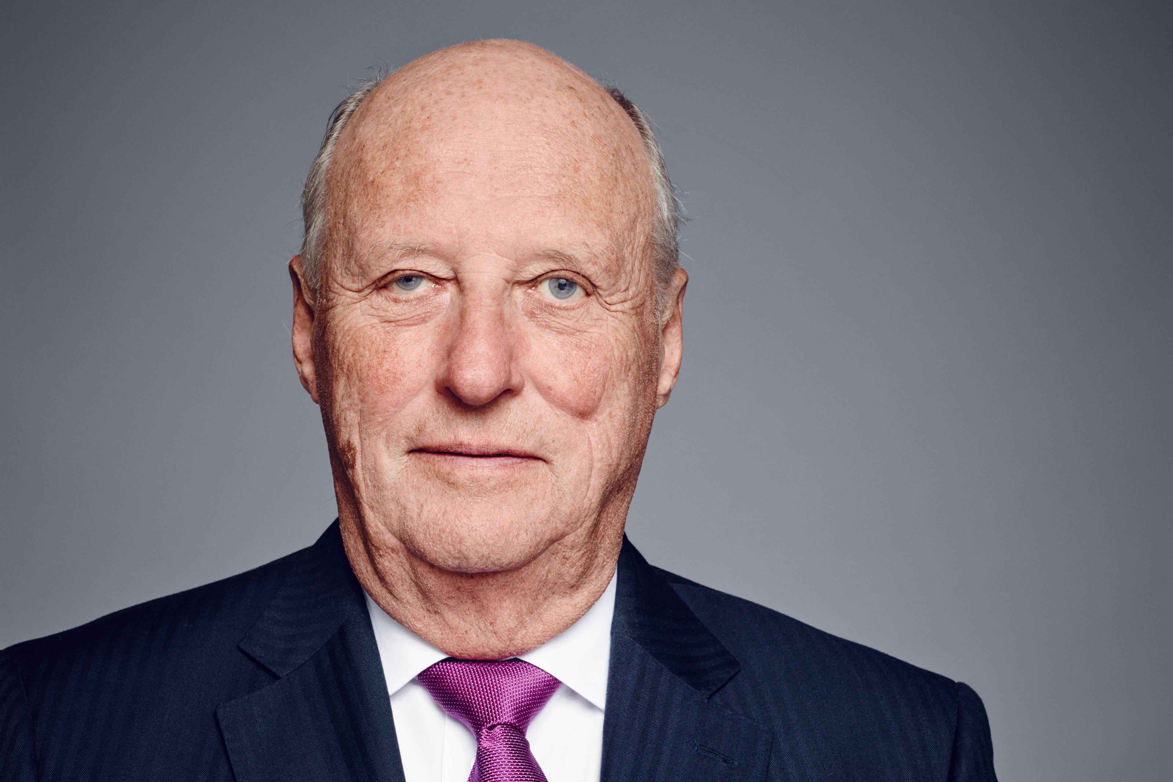 Portrett av Kong Harald i halvfigur. Kongen har mørk dress, hvit skjorte og lilla slips.