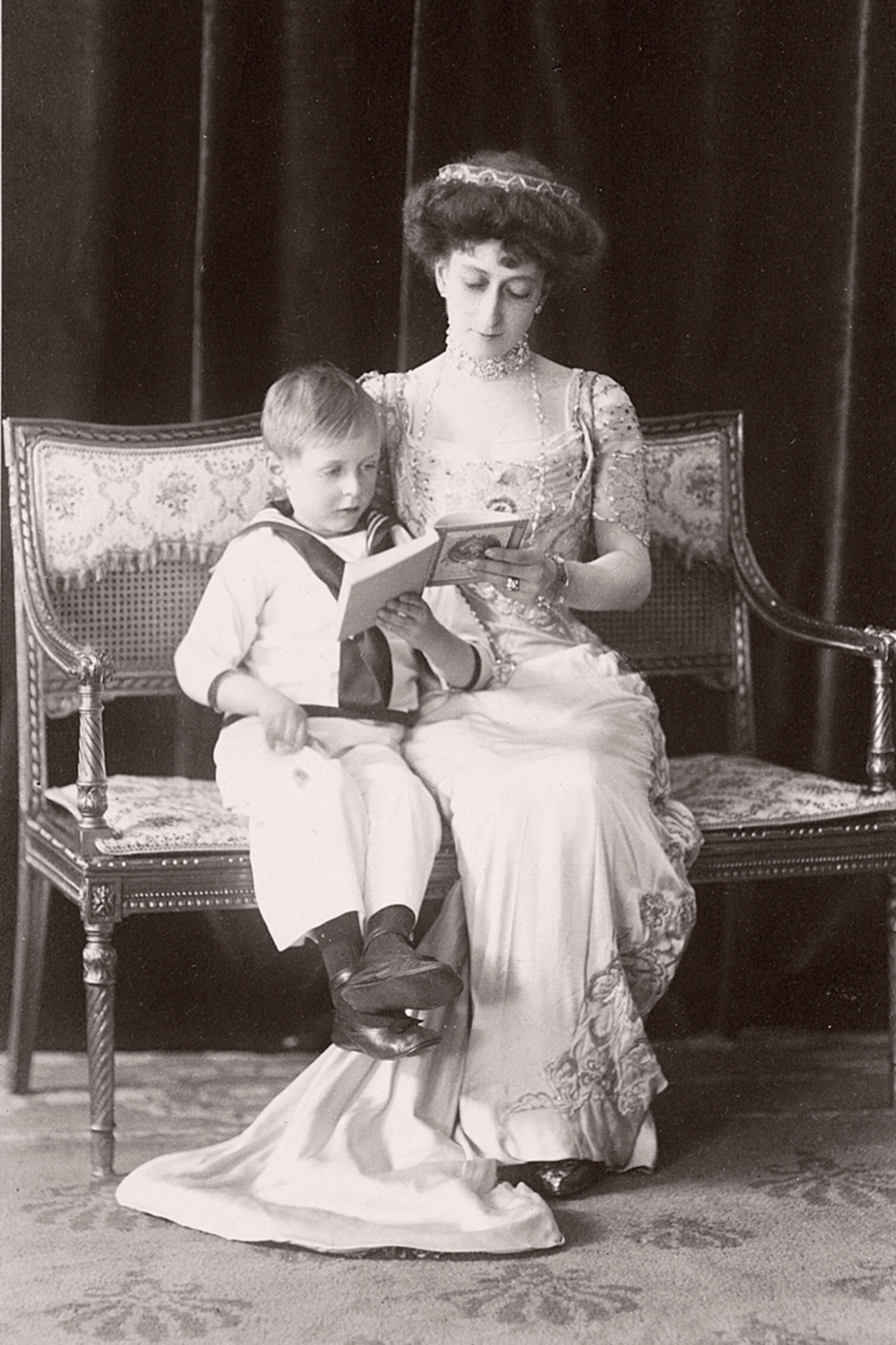 Dronning Maud og Kronprins Olav sitter sammen på en benk og leser.