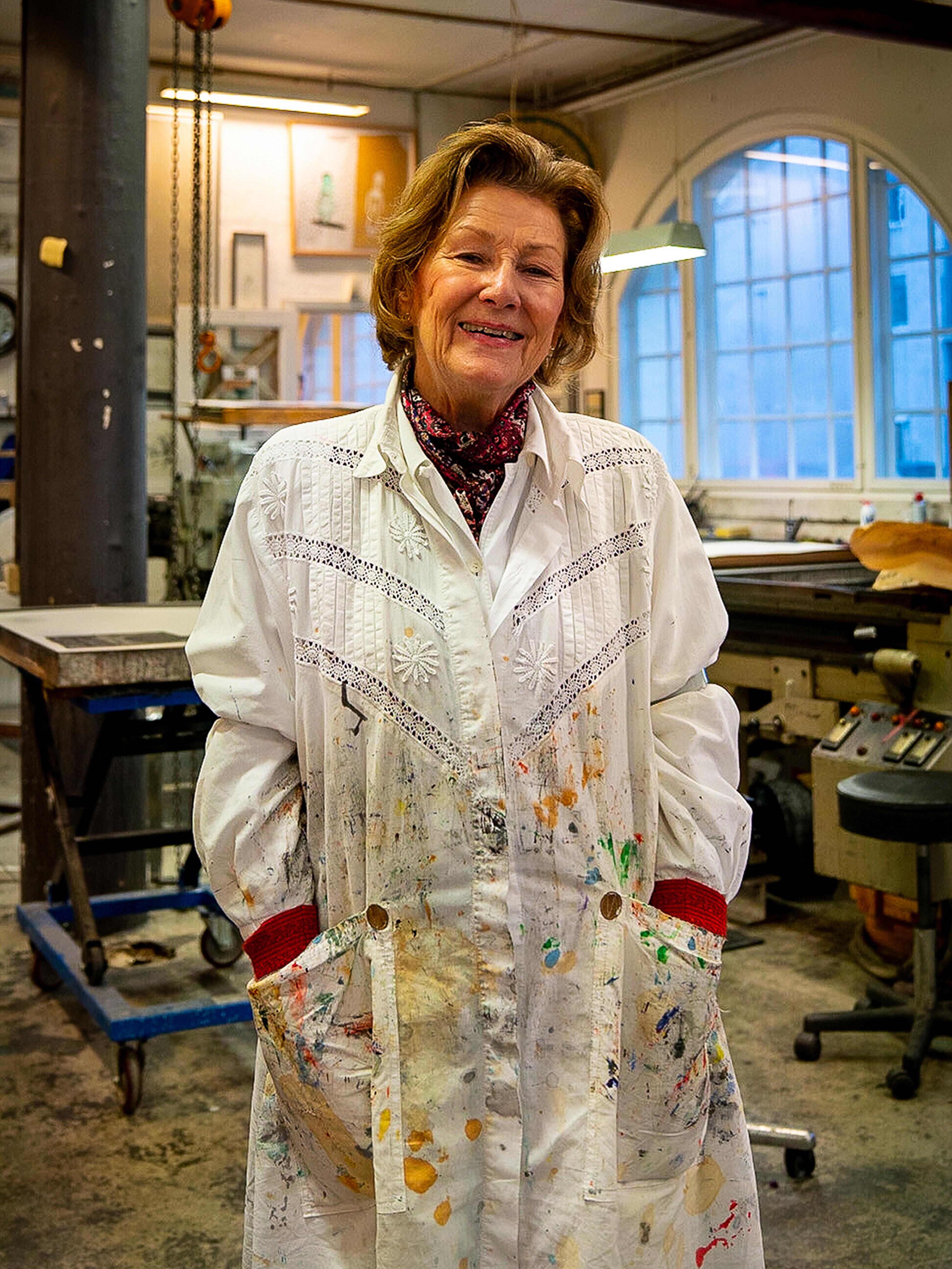 Dronning Sonja i malerantrekk med malingsflekker på.