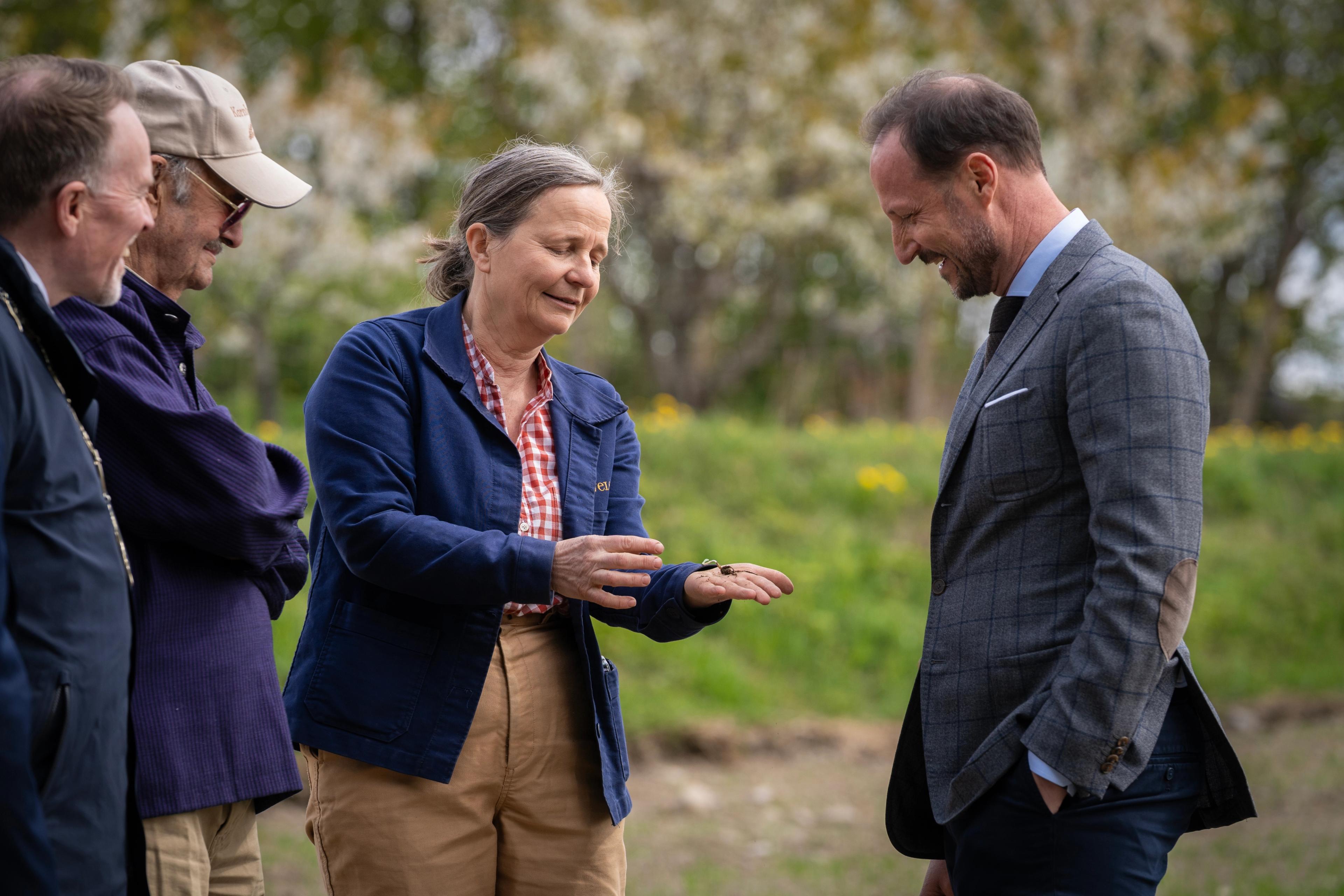 Kronprins Haakon ser ned på hånda til Marianne Olssøn der planten ligger.