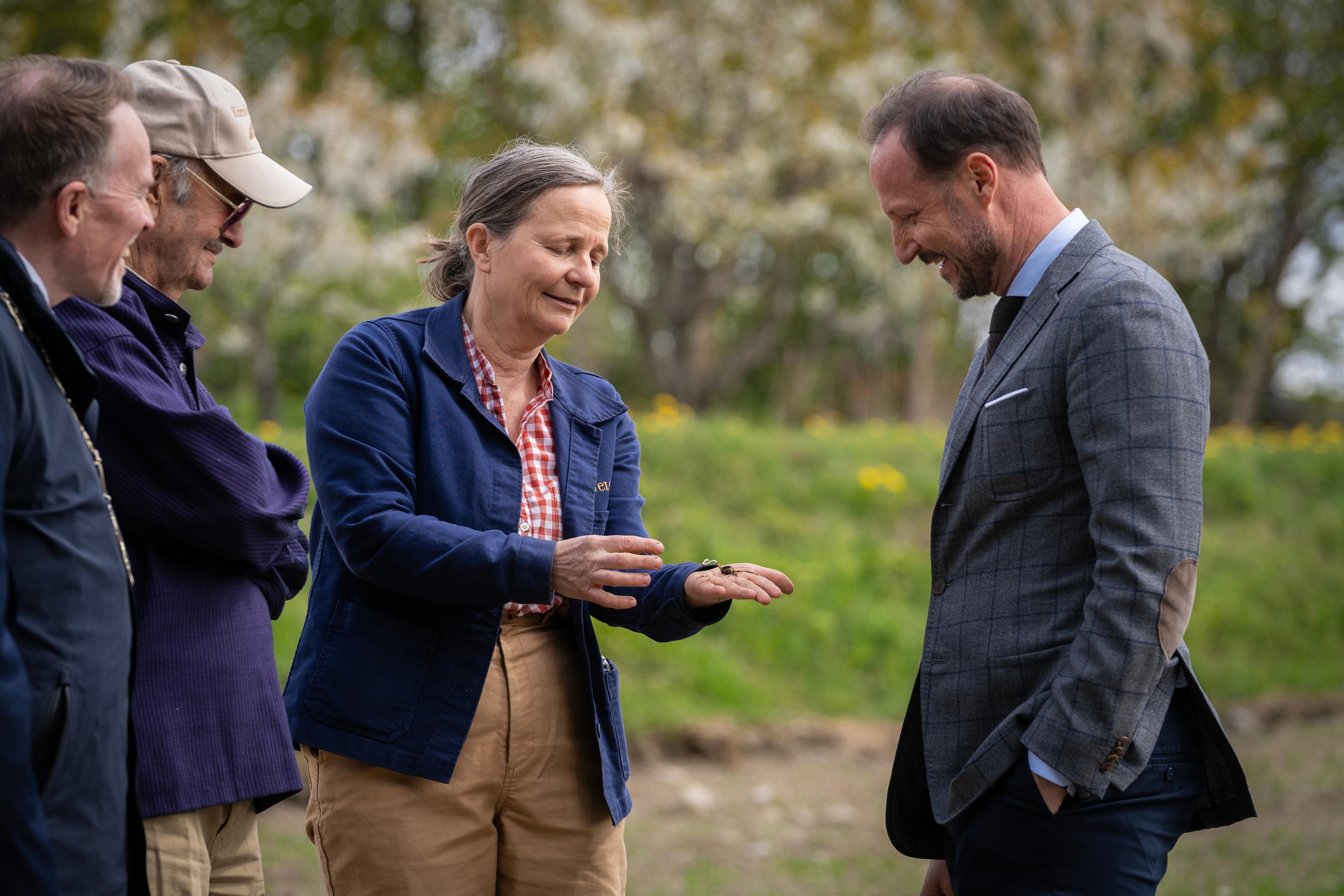 Kronprins Haakon ser ned på hånda til Marianne Olssøn der planten ligger.