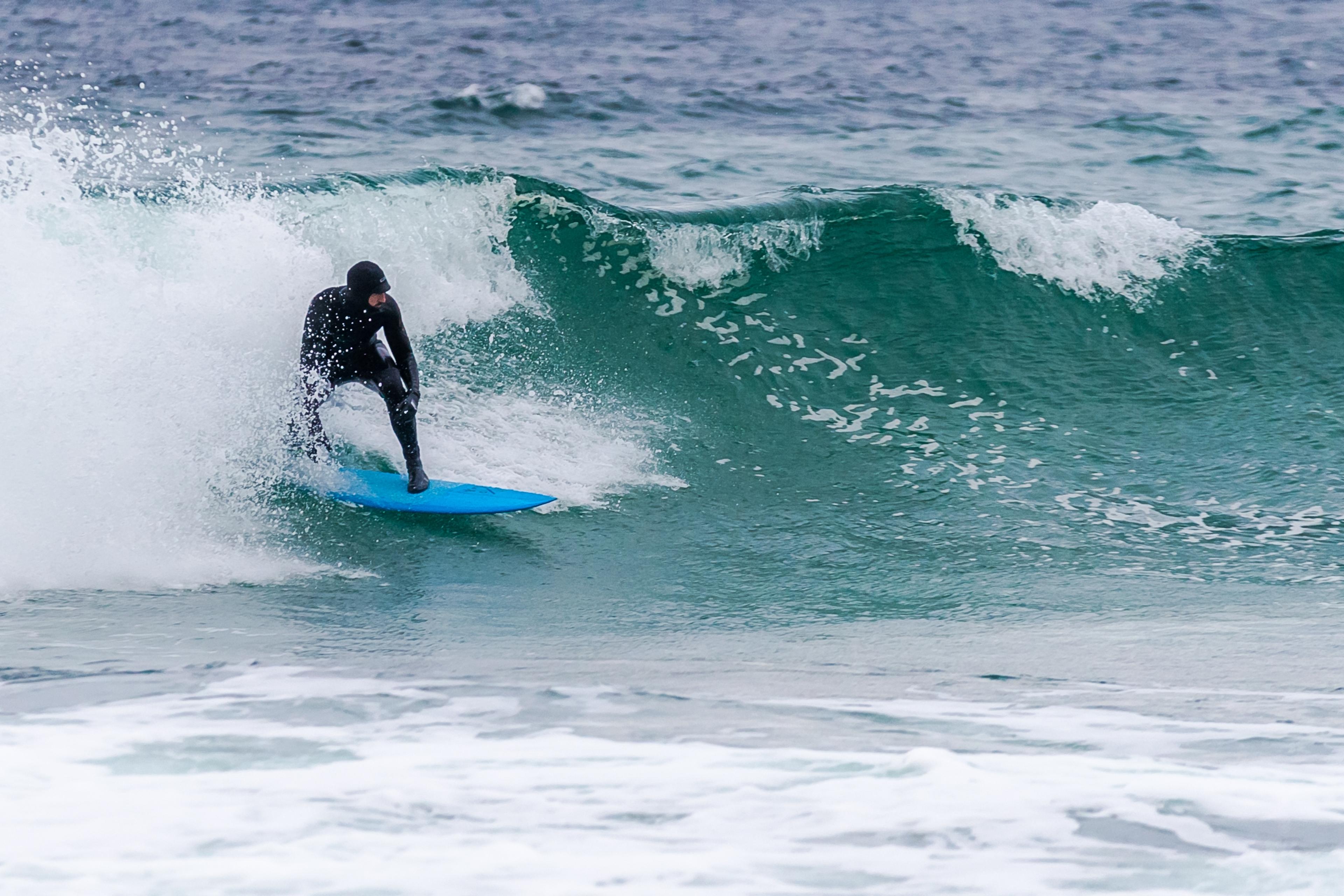 Kronprins Haakon i våtdrakt på et blått brett surfer en bølge grønt hav