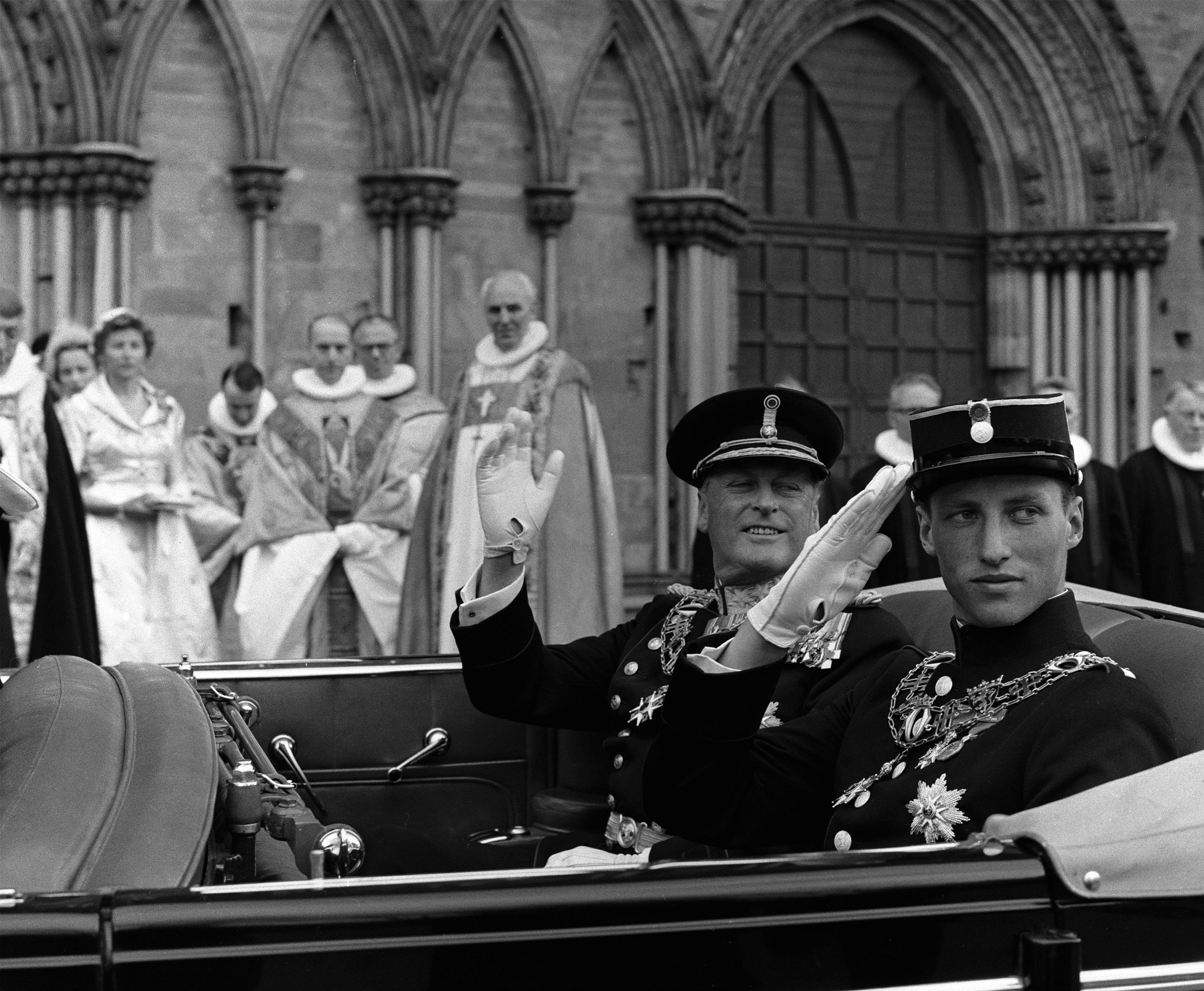 Kongen og Kronprinsen gjør honnør og vinker fra bilen. Begge er kledd i mørk gallauniform med ordener.