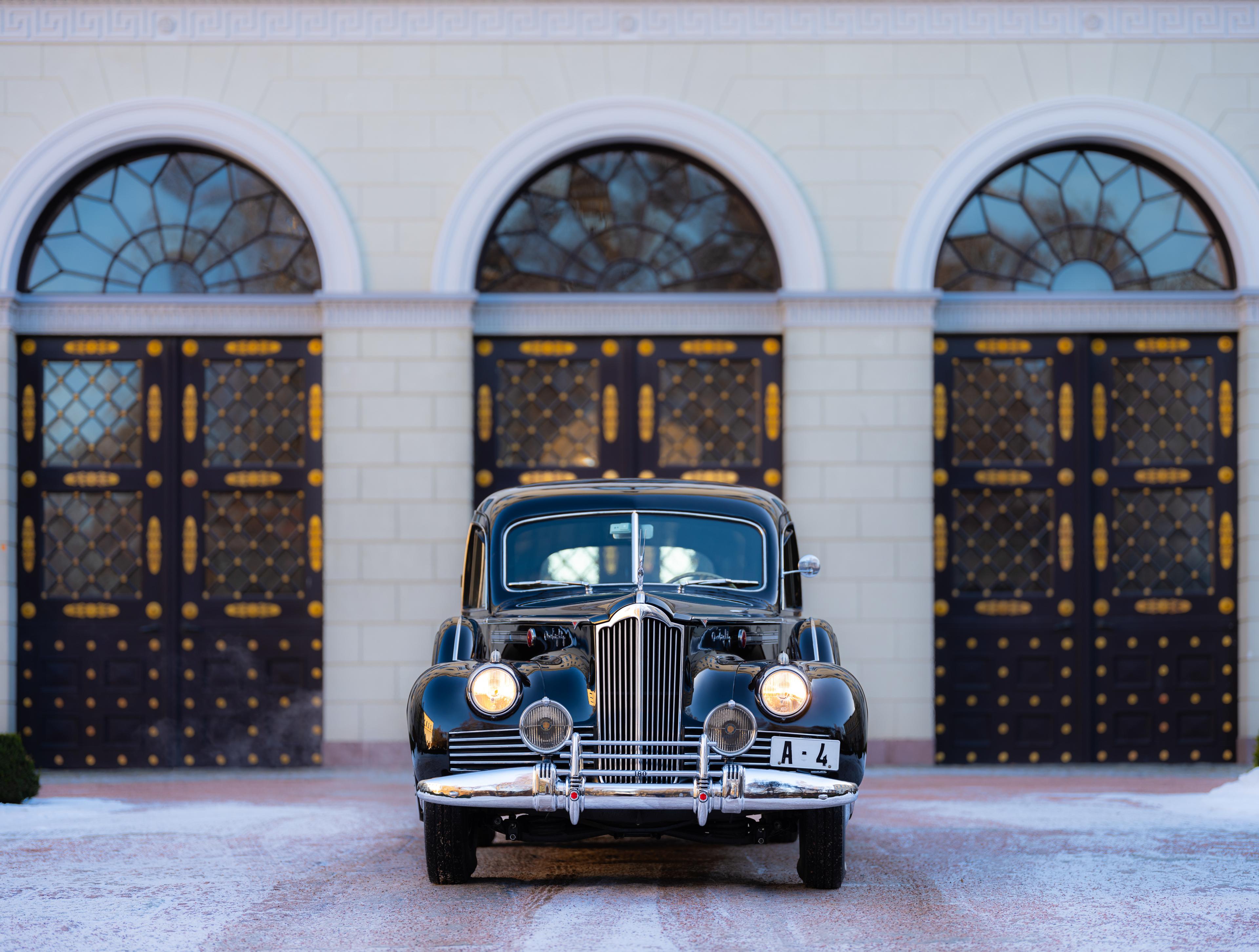En gammel, ærverdig bil med A4-skiler står parkert med fronten mot kamera. Bak skimtes Slottets fasade i Slottsgården.