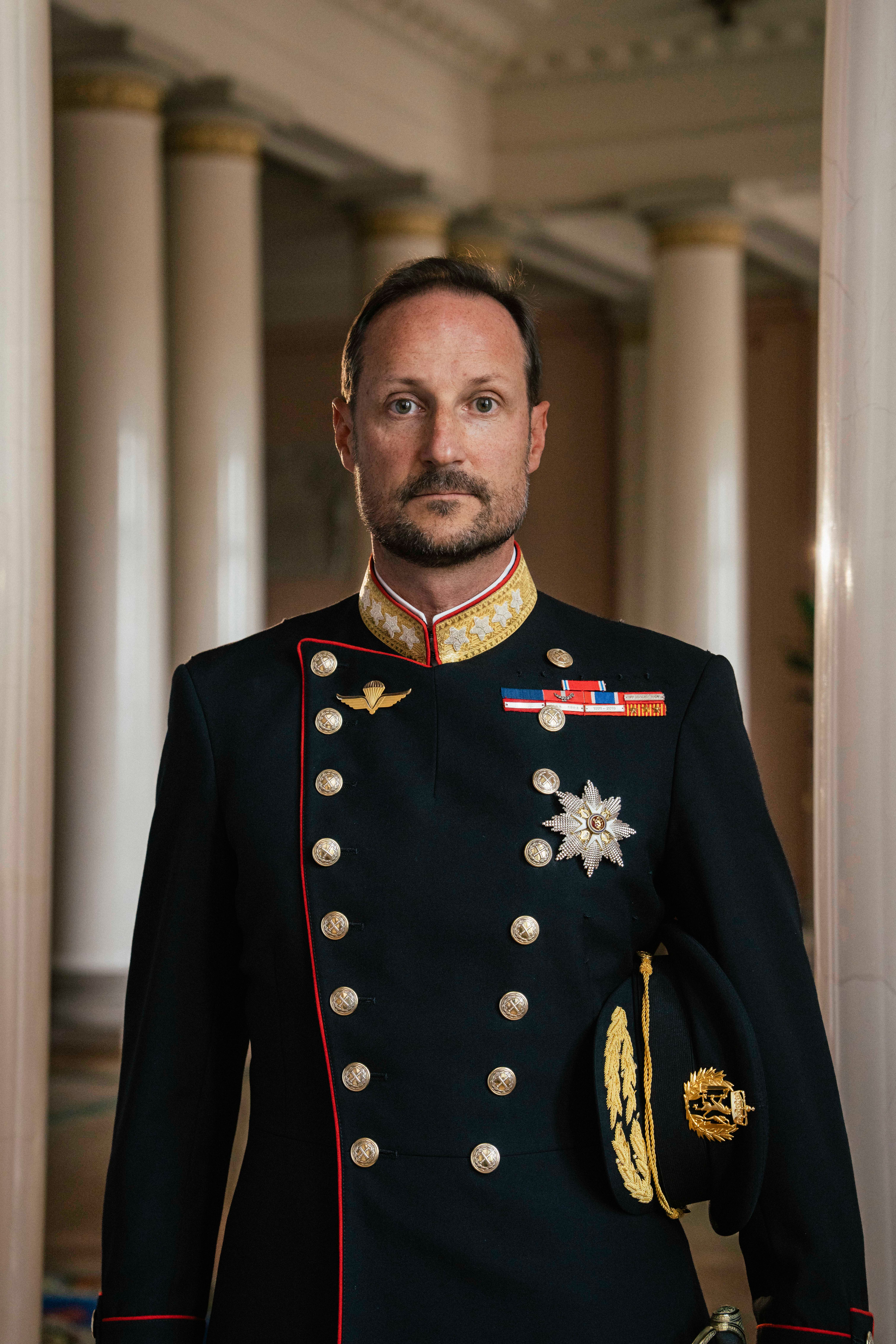 Kong Haakon stående i gallauniform med ordener og medaljer.