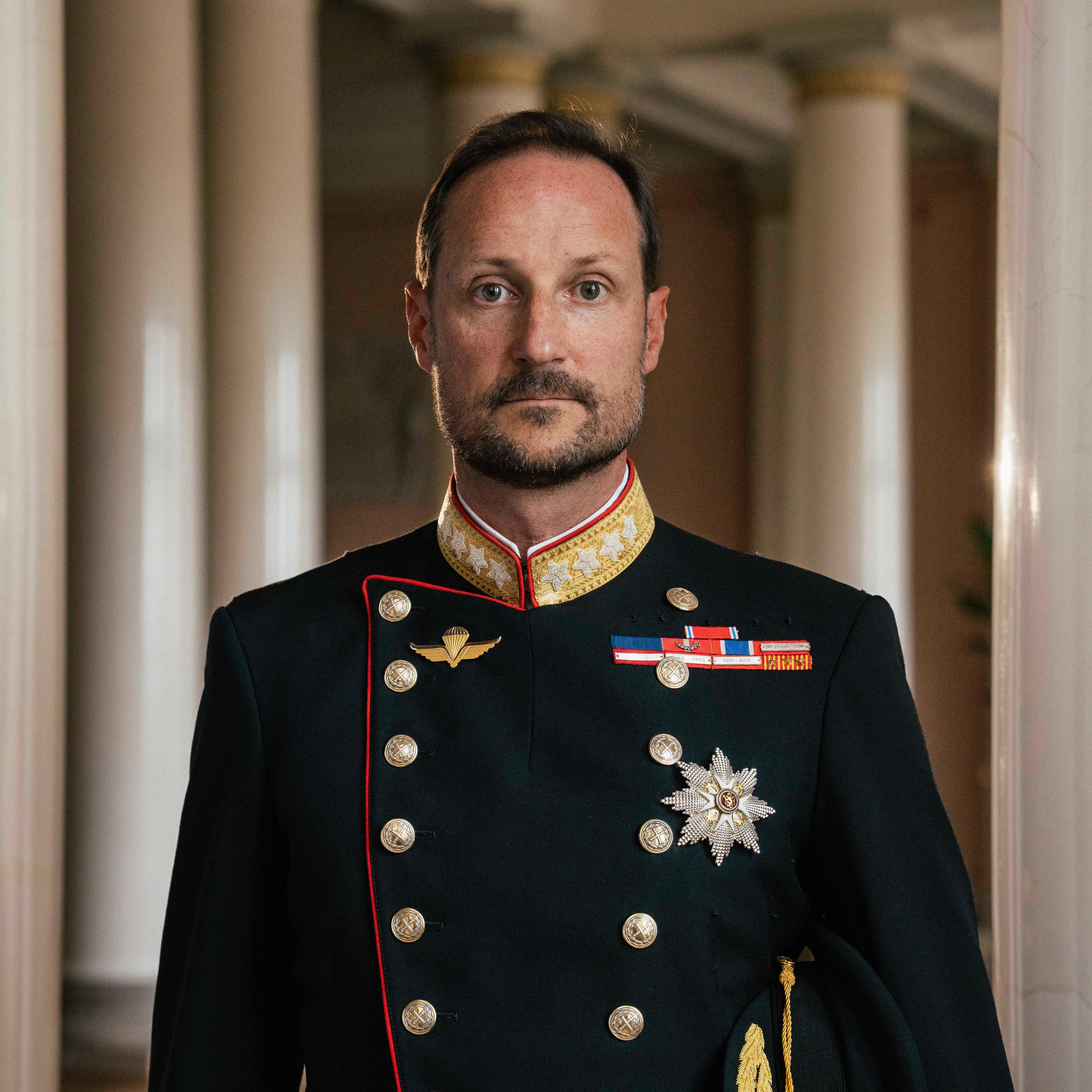 Kong Haakon stående i gallauniform med ordener og medaljer.