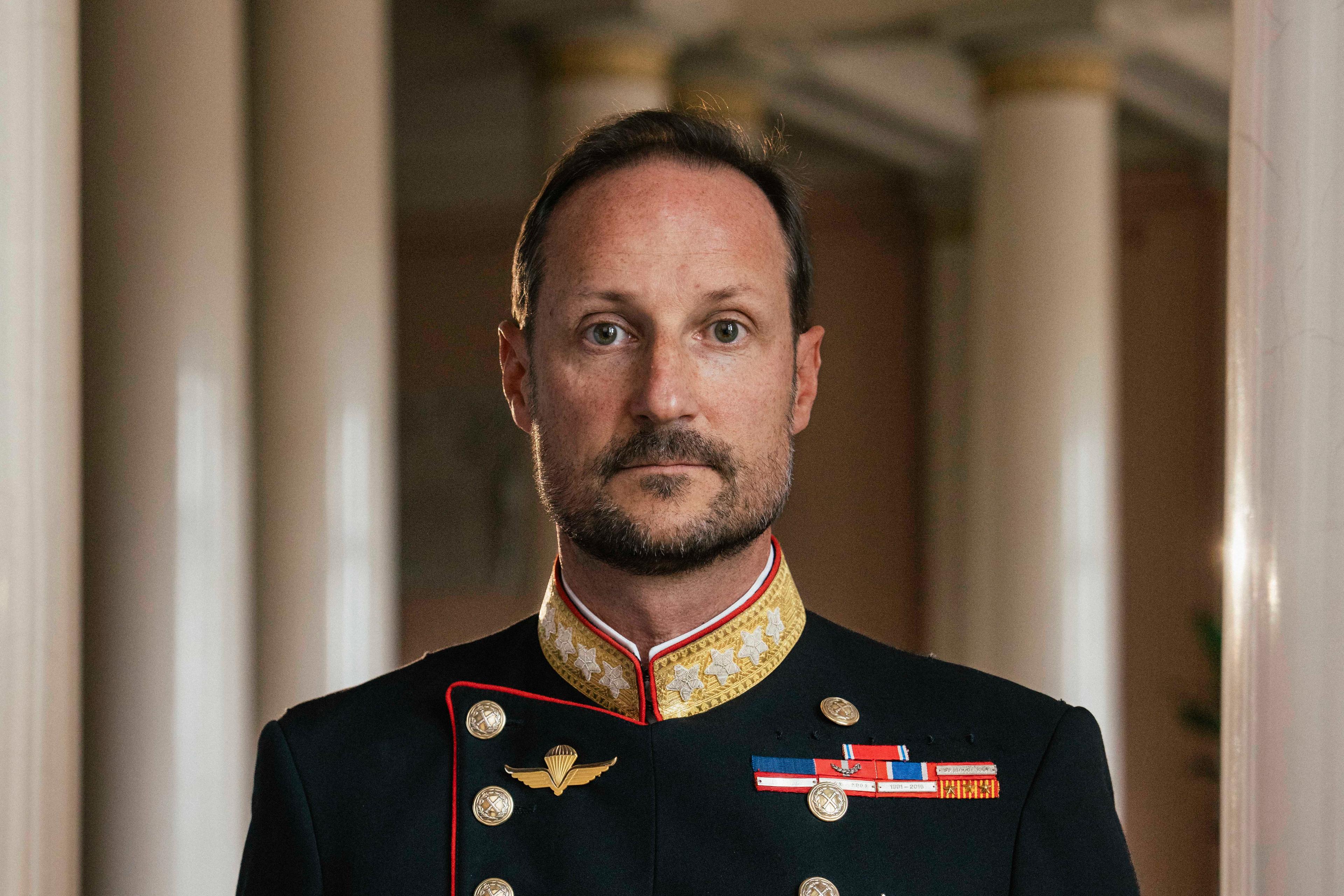 Kong Haakon stående i gallauniform med ordener og medaljer.