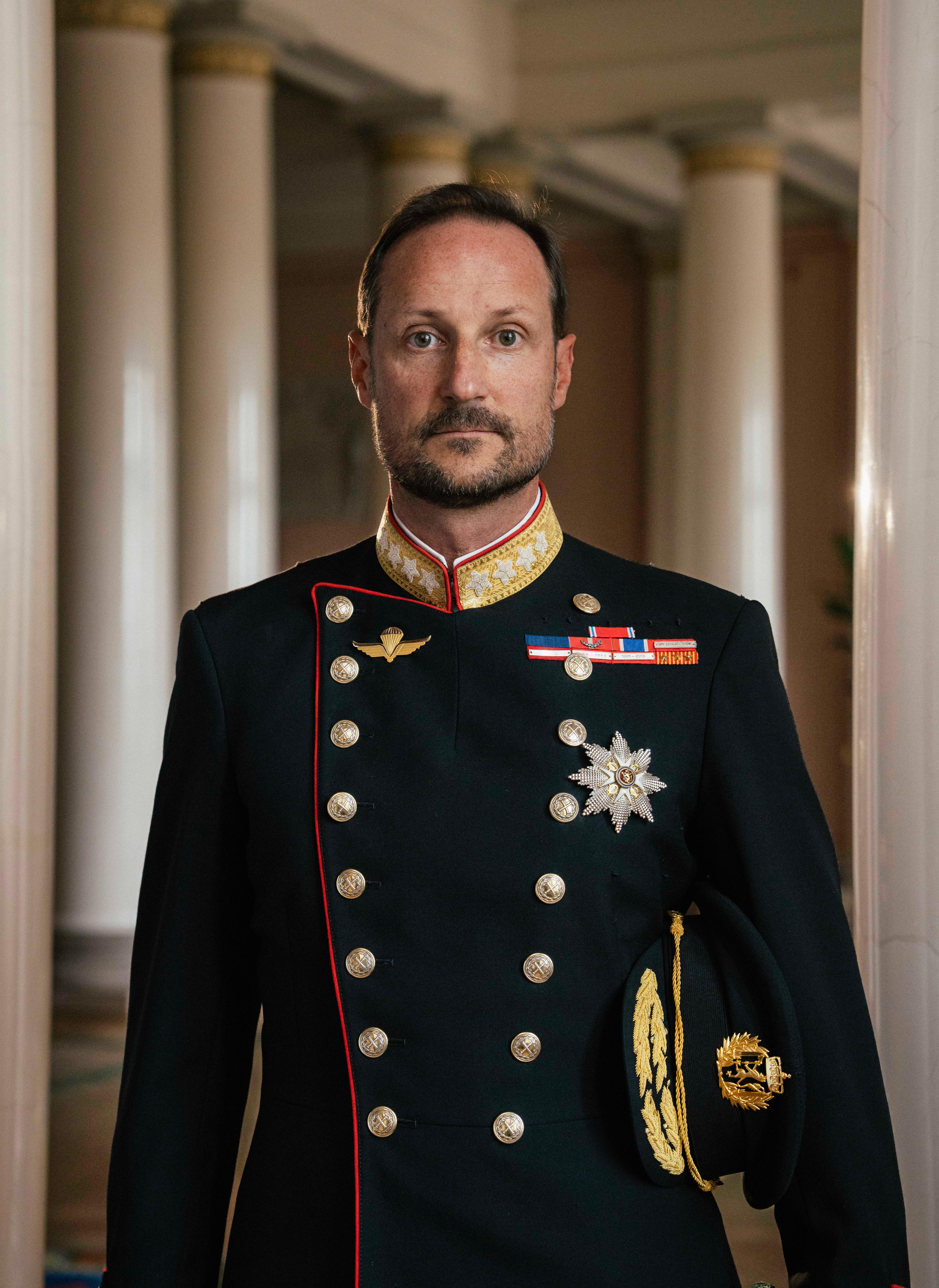 Kong Haakon stående i gallauniform med ordener og medaljer.